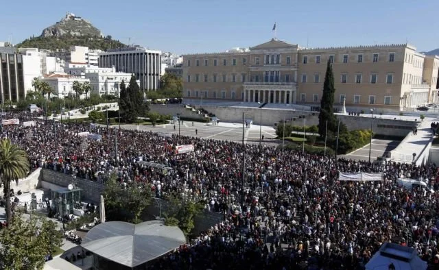 Large crowd of people gathered in front of a government building during a protest or demonstration in an urban area.