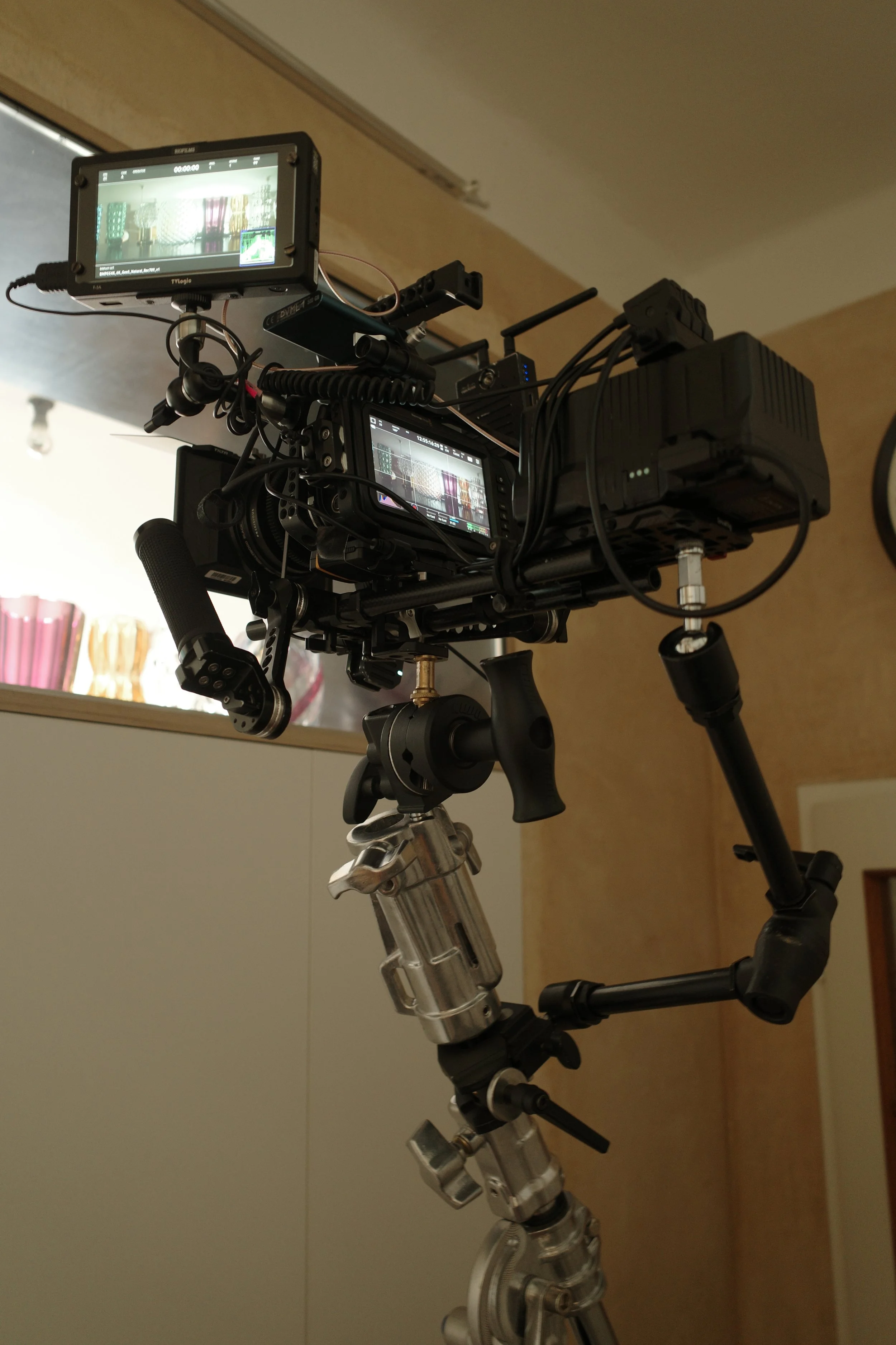 A professional video camera on a tripod, equipped with multiple monitors and cables, set up indoors.