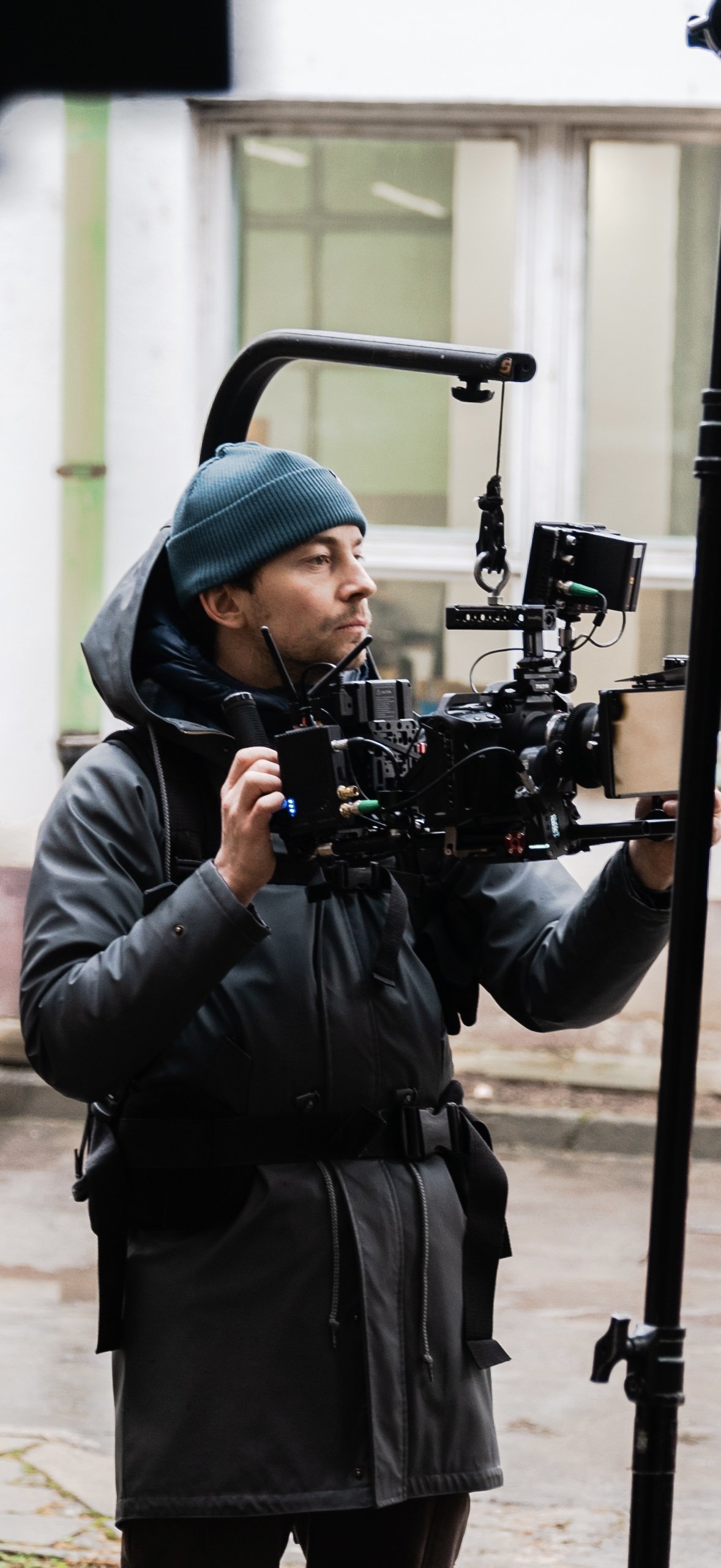 A filmmaker in outdoor clothing and a blue beanie using a professional video camera on a stabilizer rig.