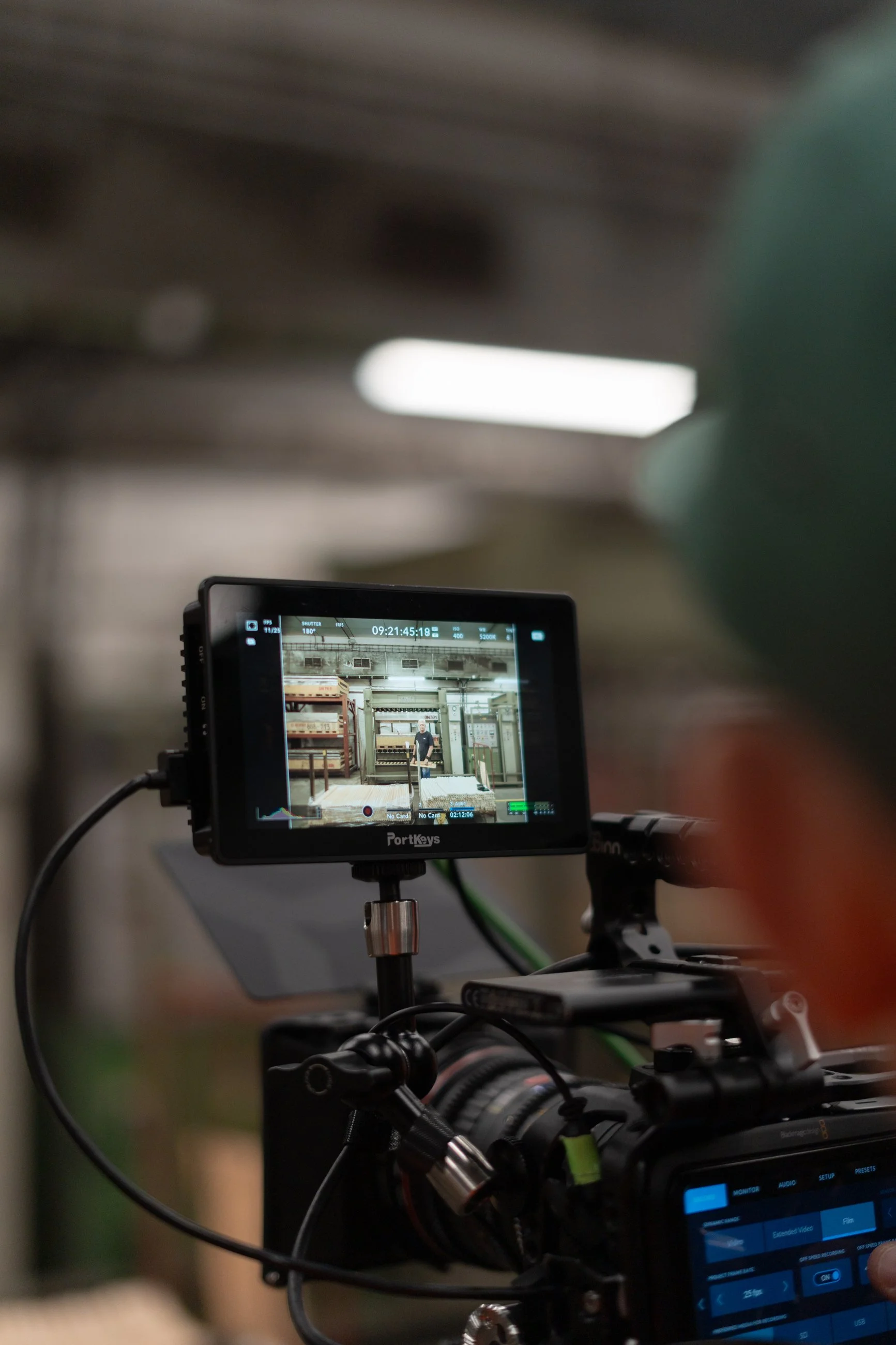 A professional video camera with a monitor displaying a shot of a person in an industrial or storage room.