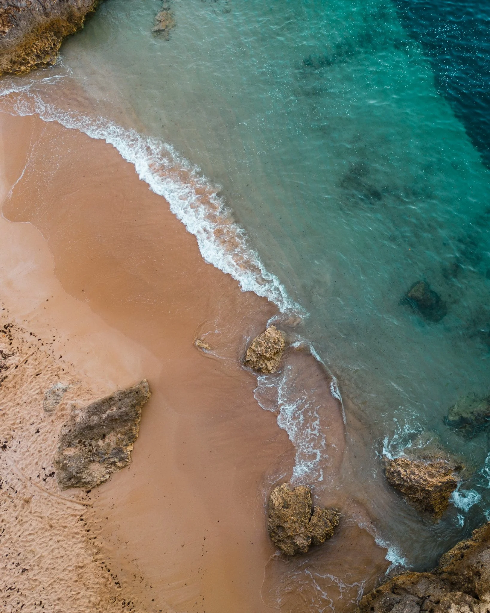Aerial view of a sandy beach with rocks and clear turquoise water.