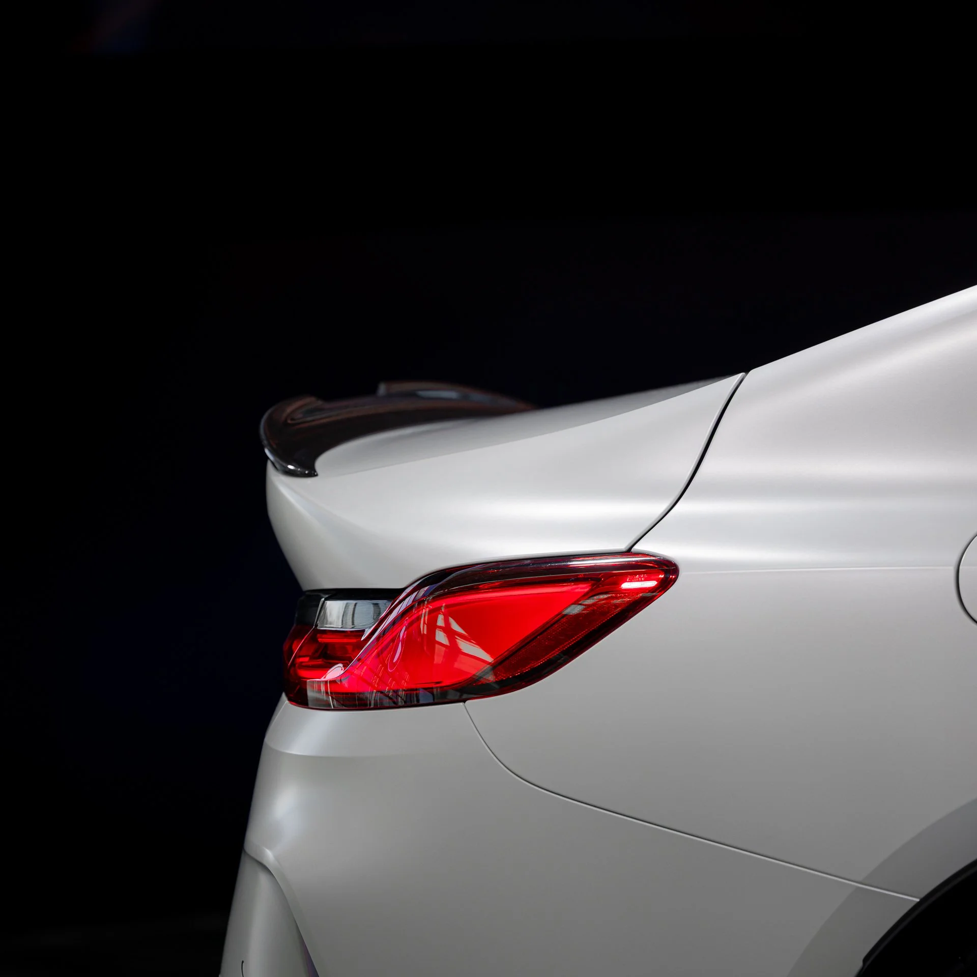 Close-up of the rear section of a white car, focusing on the taillight and part of the trunk, against a black background.