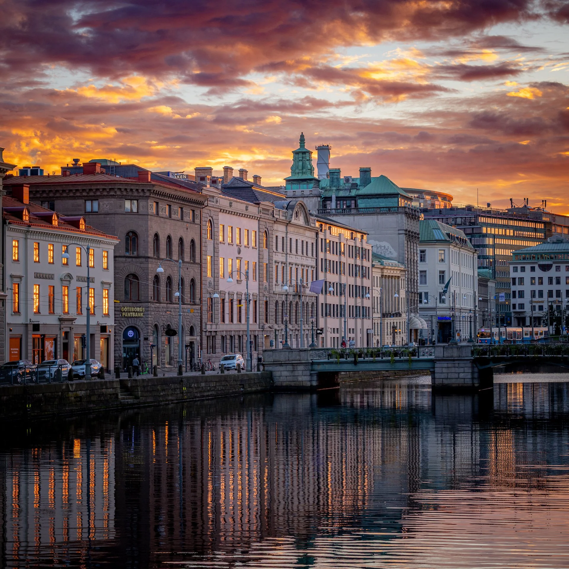 Sunset over city buildings with reflections in the river below.