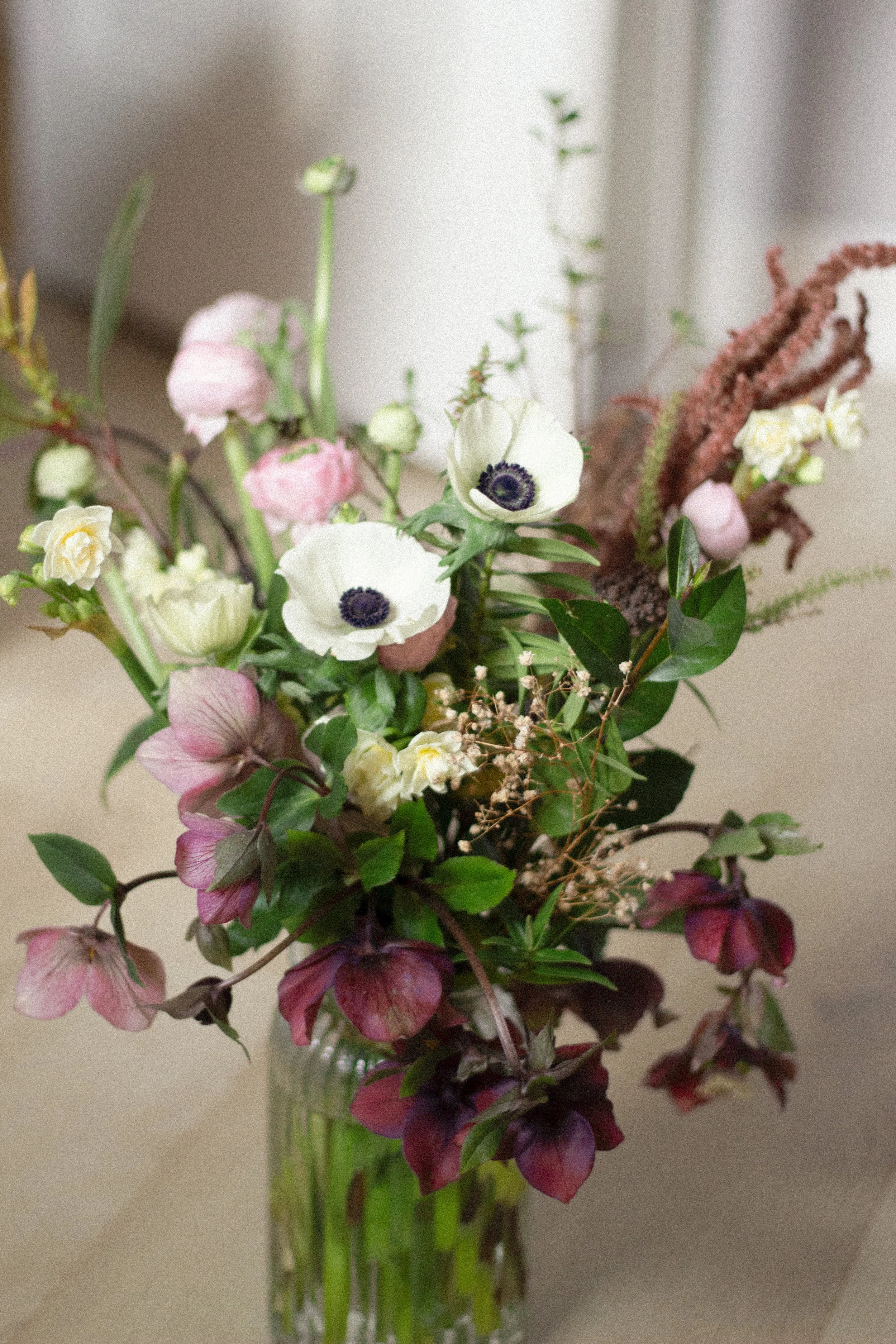A floral arrangement in a glass vase, consisting of anemone flowers, pink and white blooms, and greenery.