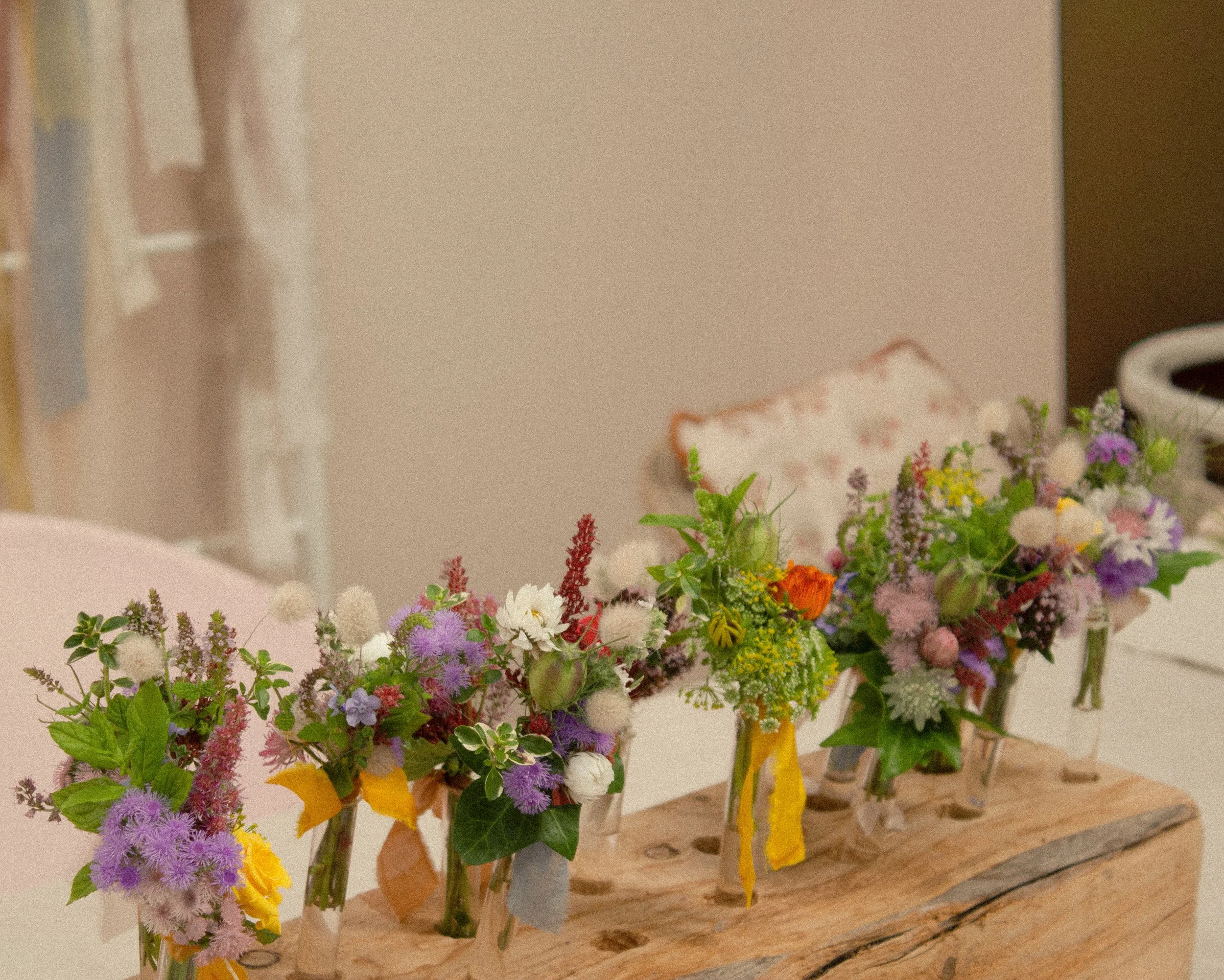 Close-up view of colorful flower buttonholes for a wedding arranged in vases on a wooden table, with a plain background.