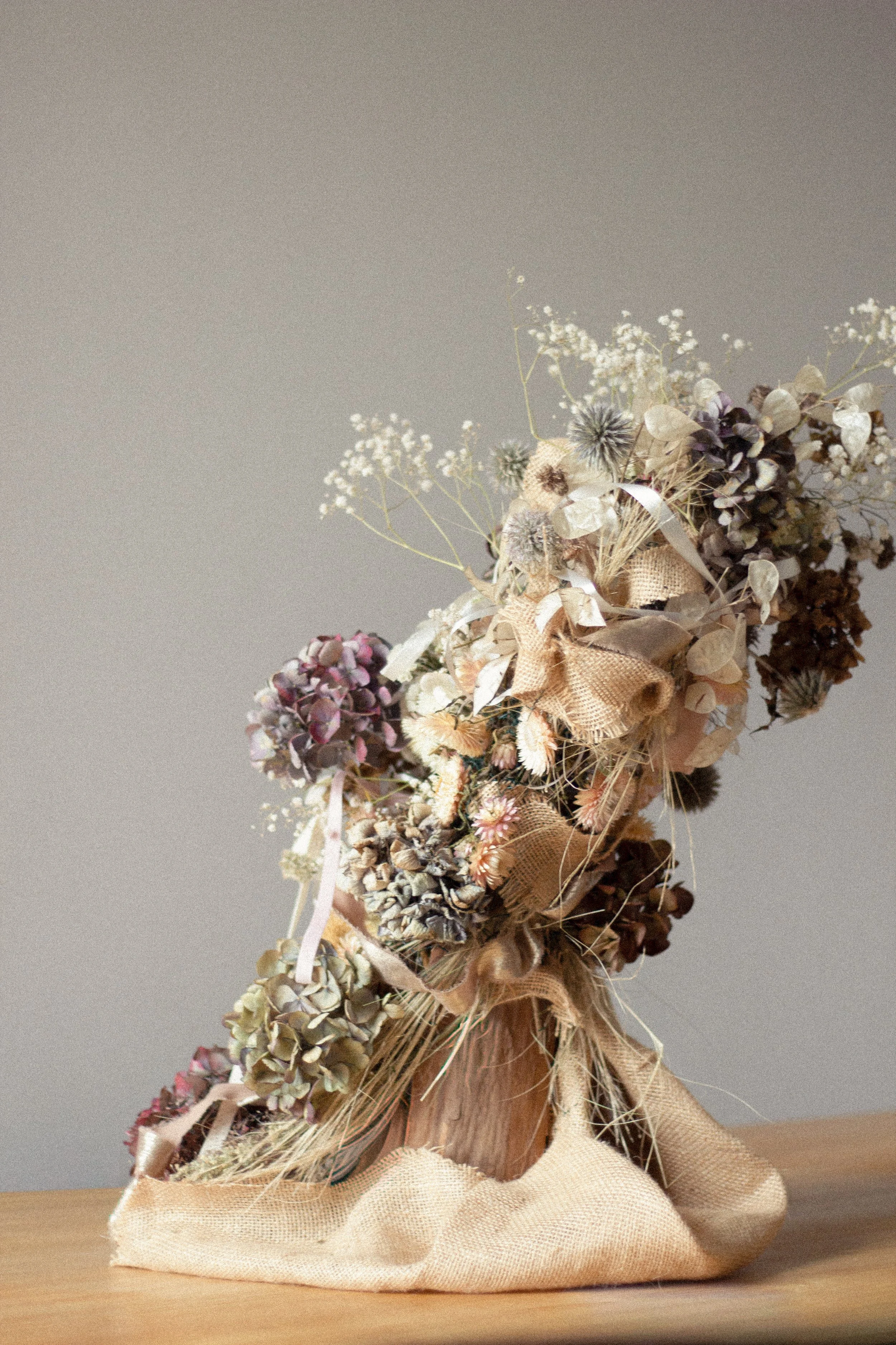 Sculpture of dried flowers and plants wrapped in burlap and ribbon, placed on a wooden surface.