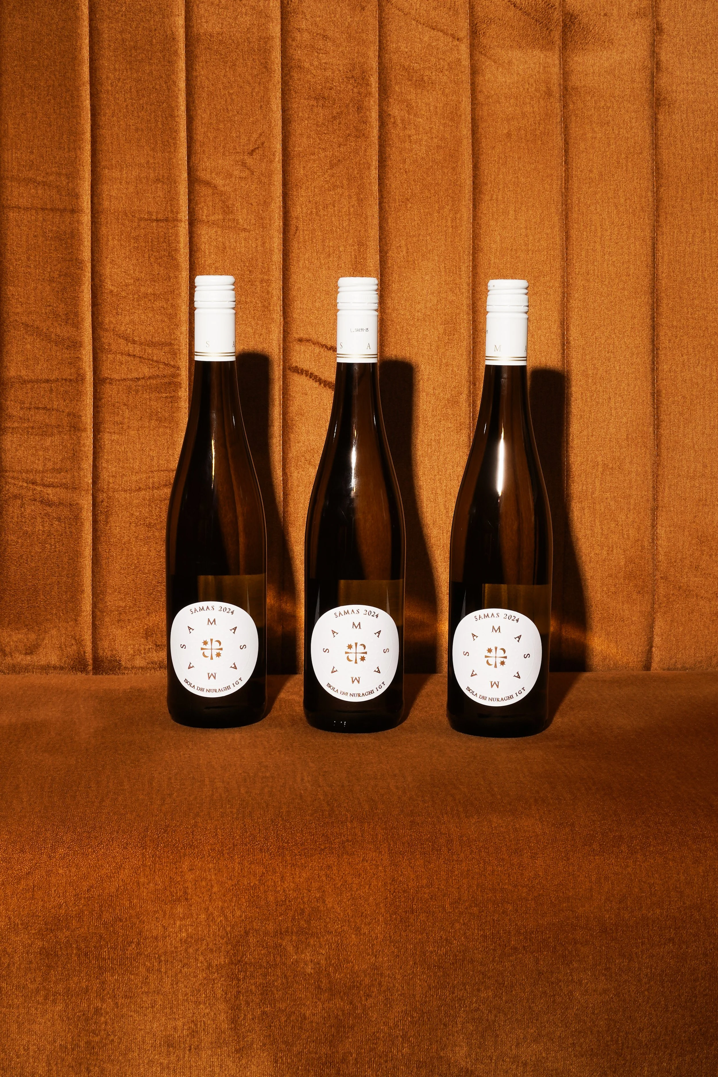 Trois bouteilles de vin posées sur une surface en bois, avec un rideau orange en arrière-plan.