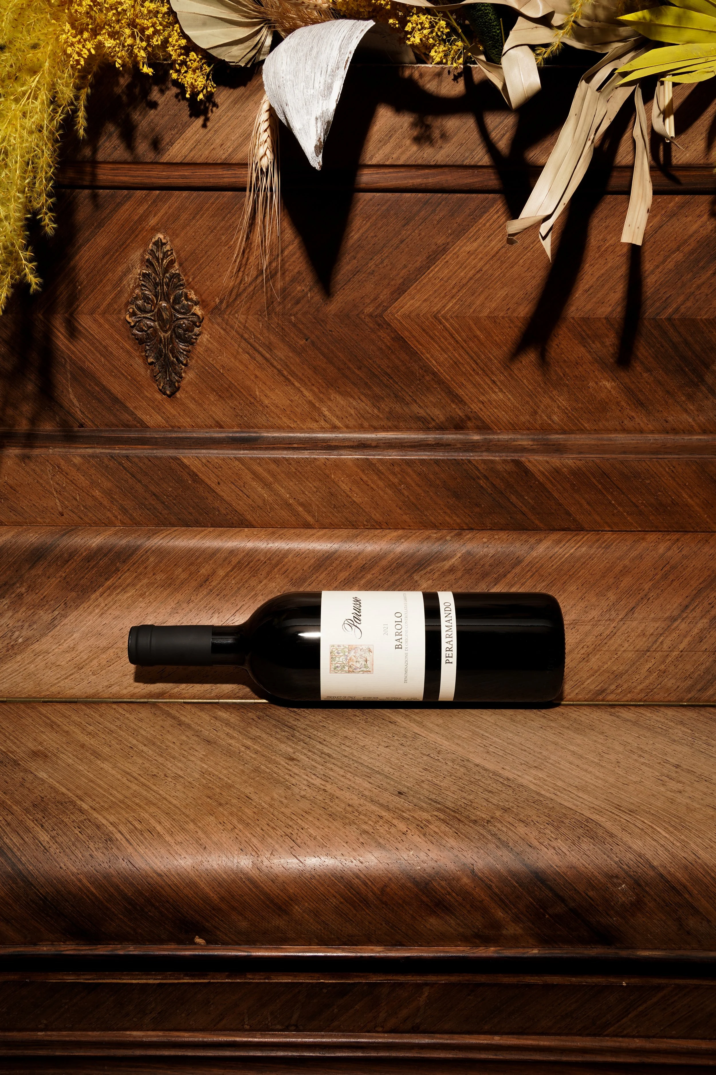 Une bouteille de vin rouge reposant sur une surface en bois, avec des fleurs séchées et des plantes en décoration en arrière-plan.