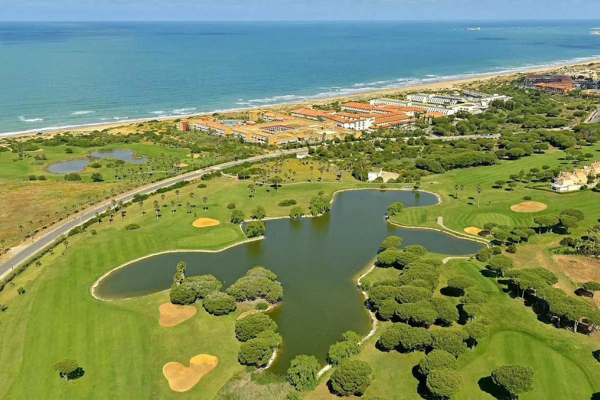 Aerial view of a golf course near the ocean with lakes, trees, sand bunkers, and green fairways.
