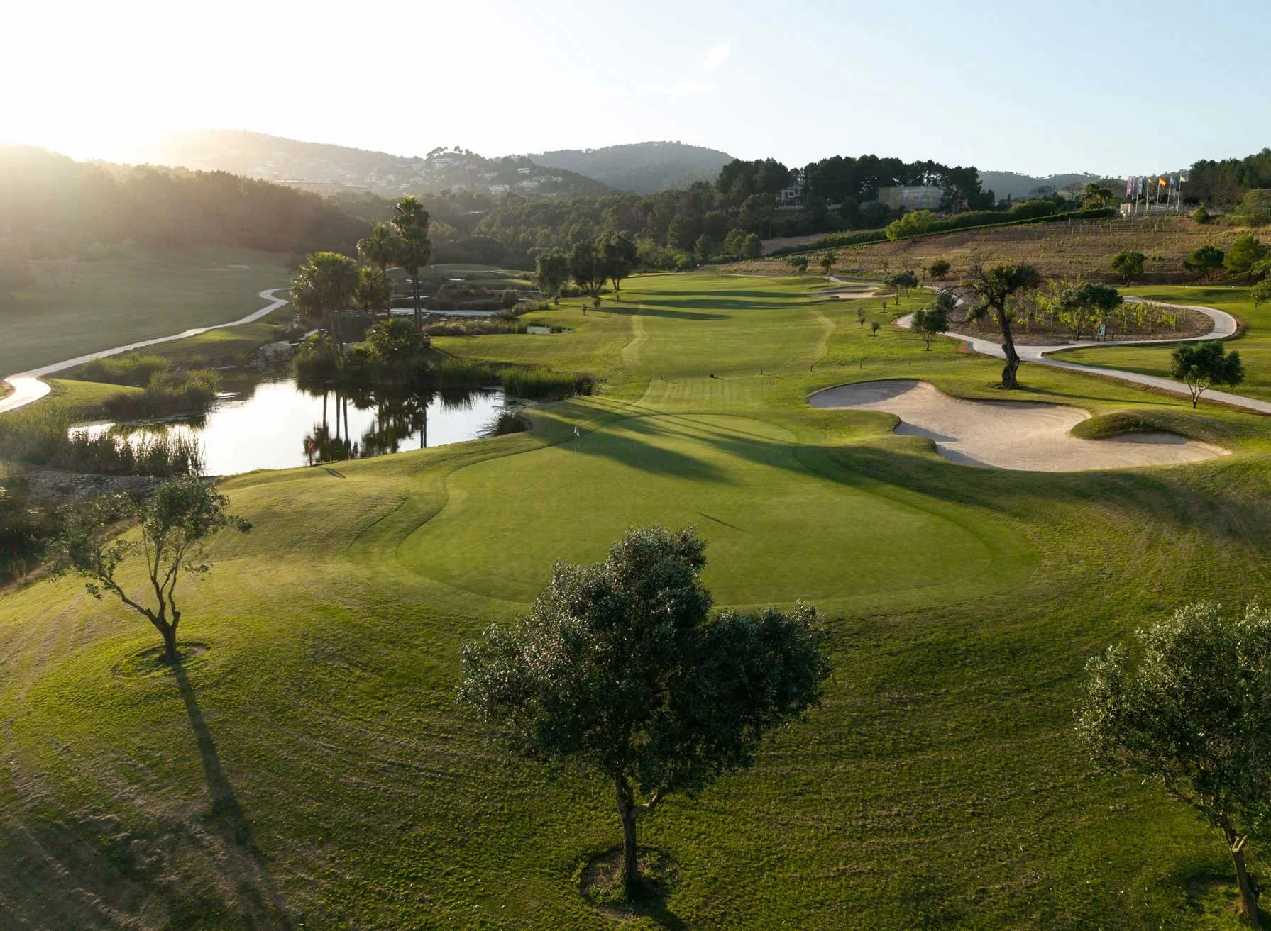 Fairway, trees and lake at Arabella Golf Mallorca in late-afternoon light, with hills behind