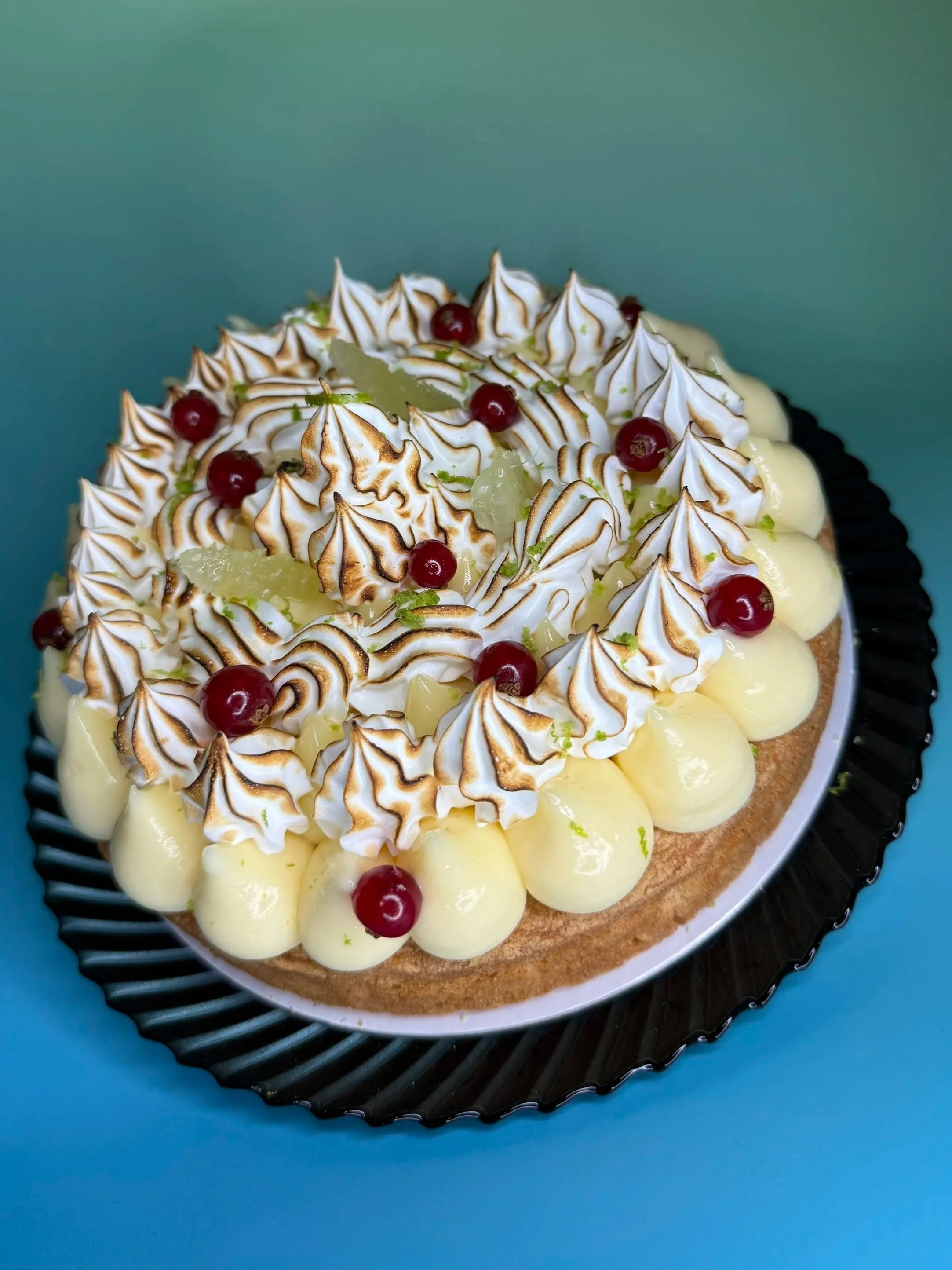 Gâteau décoré avec des meringues grillées, des groseilles, des morceaux de citron, et de la crème sur une assiette noire