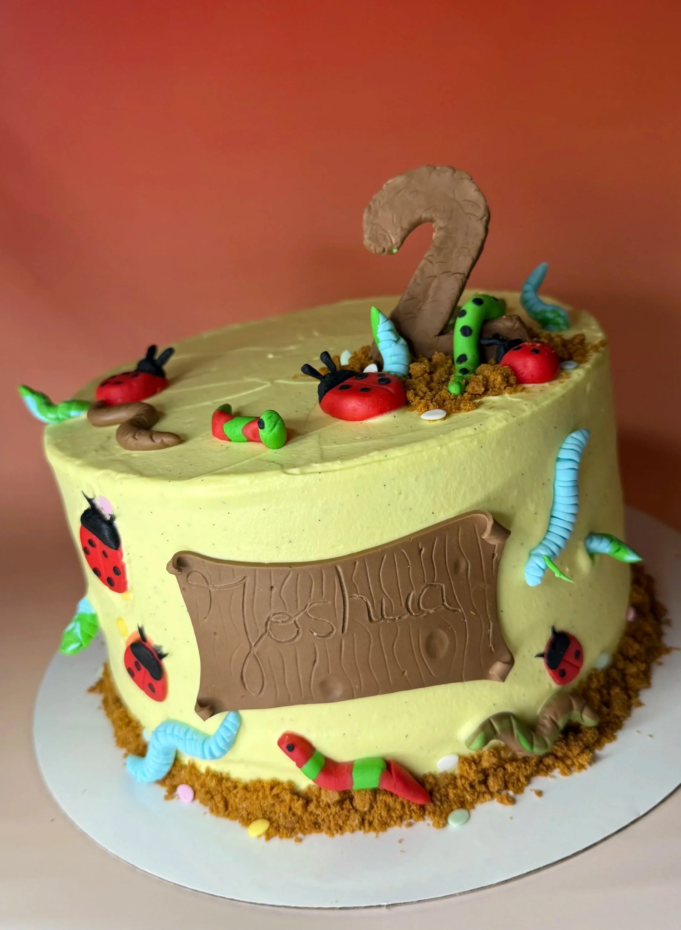Gâteau d'anniversaire jaune décoré avec des figurines de petites chenilles et coccinelles, un numéro 2 en chocolat en haut.