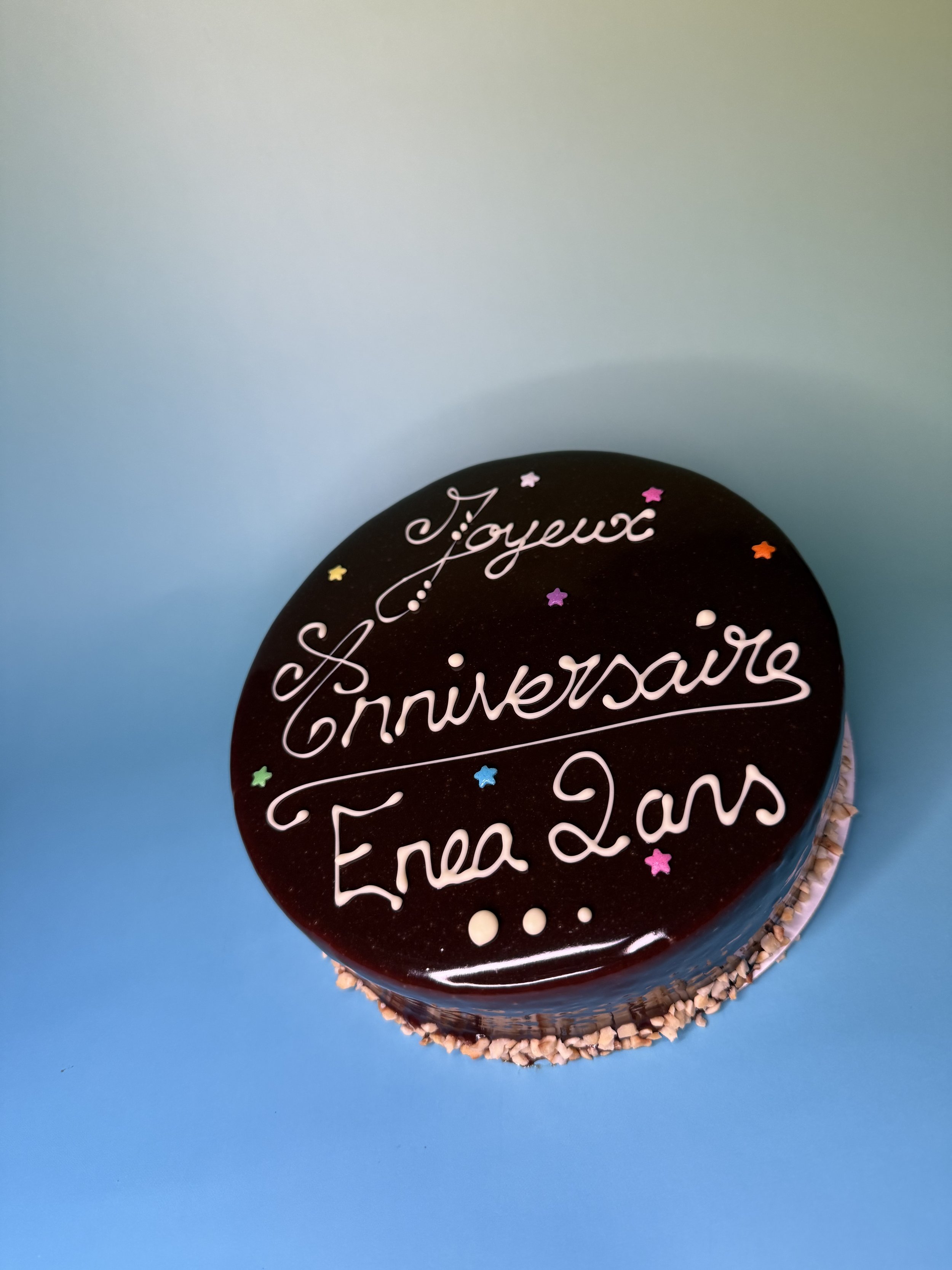 Gâteau anniversaire avec inscription en français et décorations de petites étoiles colorées, placé sur un fond bleu