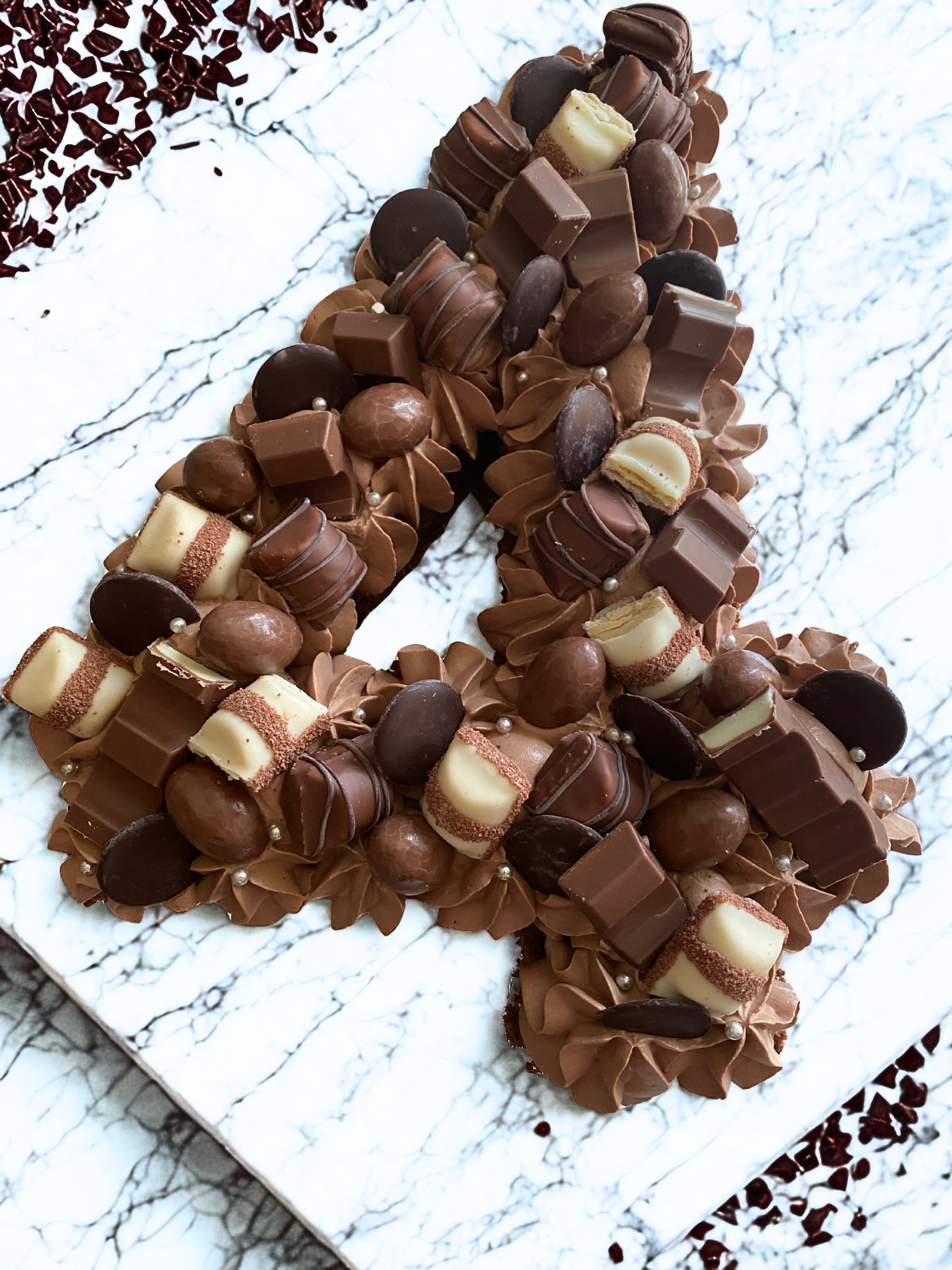 Gâteau en forme de chiffre 1 décoré avec des chocolats et des coupelles en chocolat, posé sur une surface blanche avec un motif de veines noires.