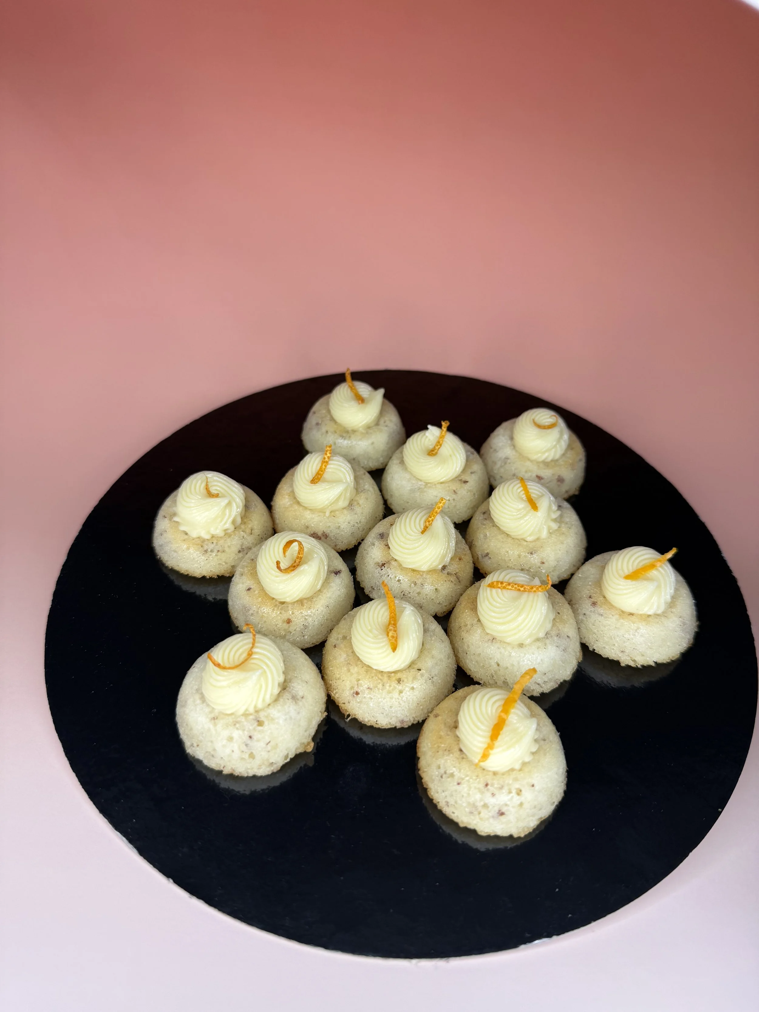 Petits gâteaux ronds avec une ganache blanche décorée d'une fine bande orange en haut, disposés sur un plateau noir.