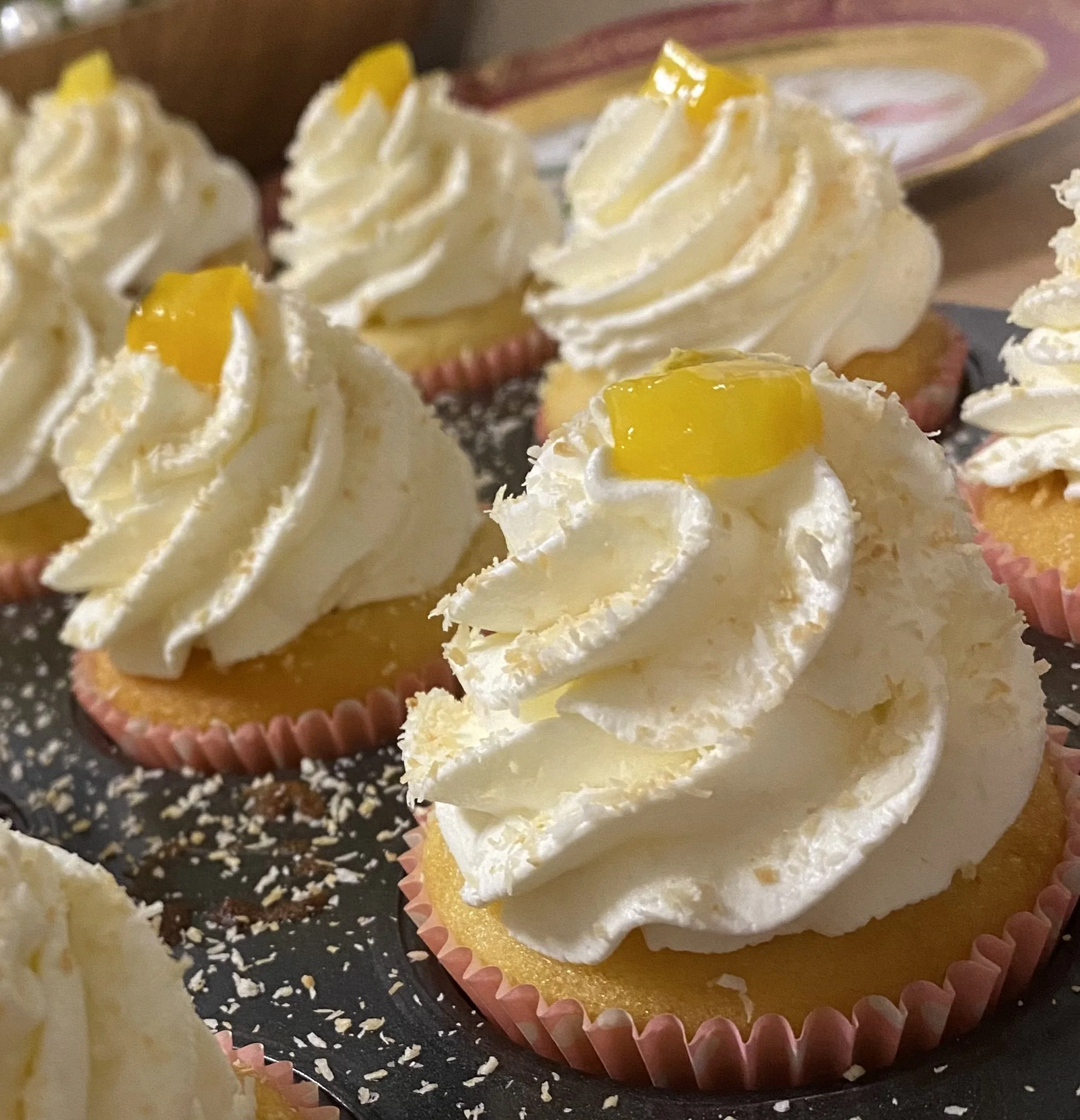 Petits cupcakes avec crème fouettée et morceaux de mangue dessus, dans des caissettes en papier rose.