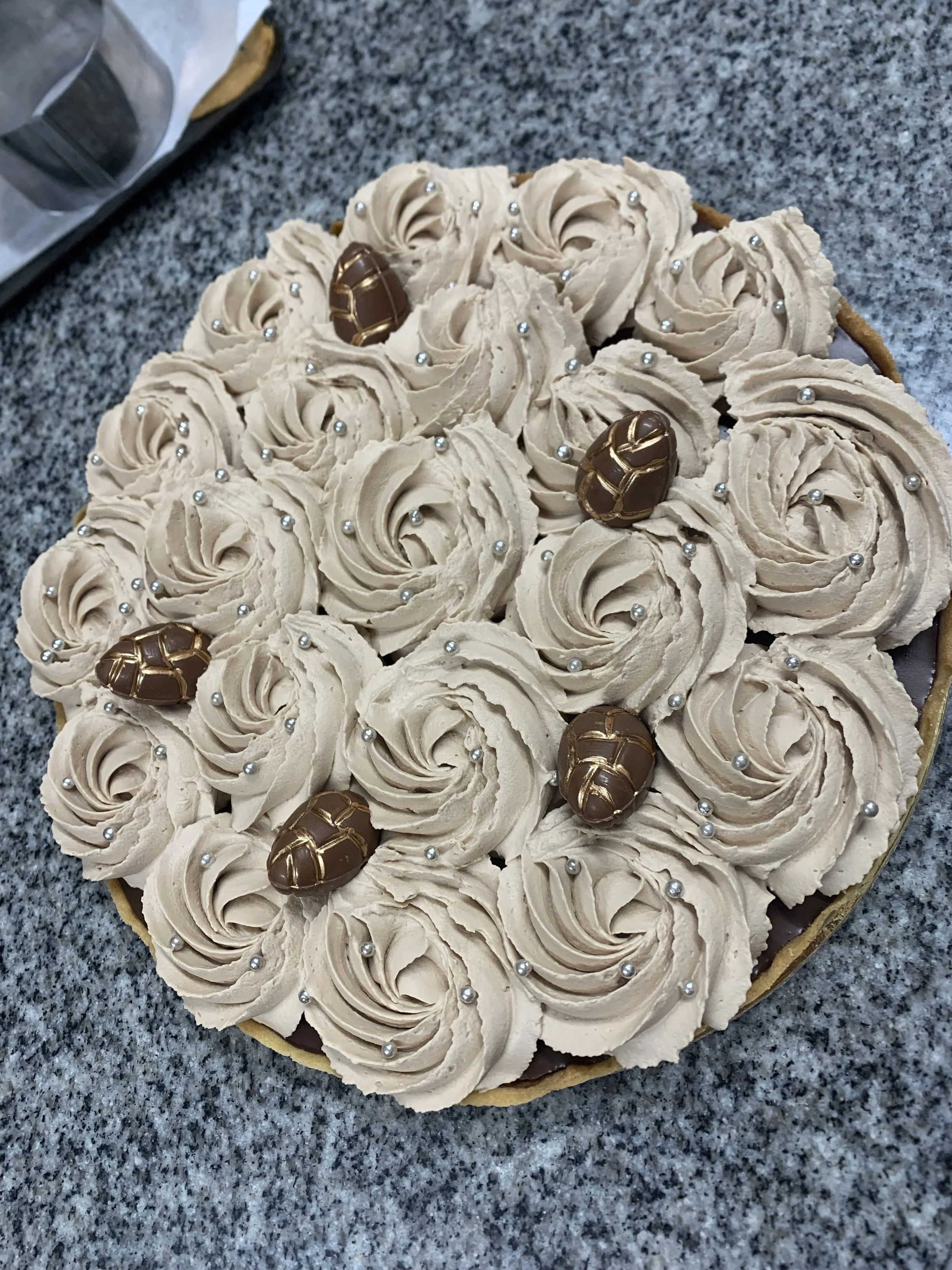 Gâteau rond décoré de crème au beurre ou de chantilly, ornée de petits perles argentées et de quelques œufs en chocolat en forme de coquillage doré