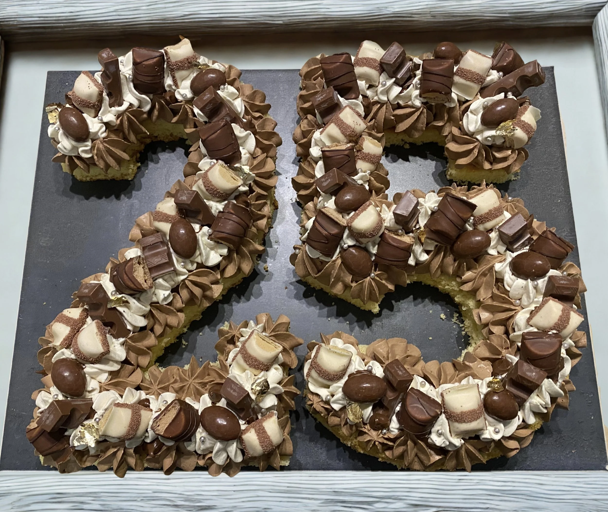 Gâteau en forme de chiffres 20 décoré avec des morceaux de chocolat, des pipings de crème au chocolat, et des petits biscuits.