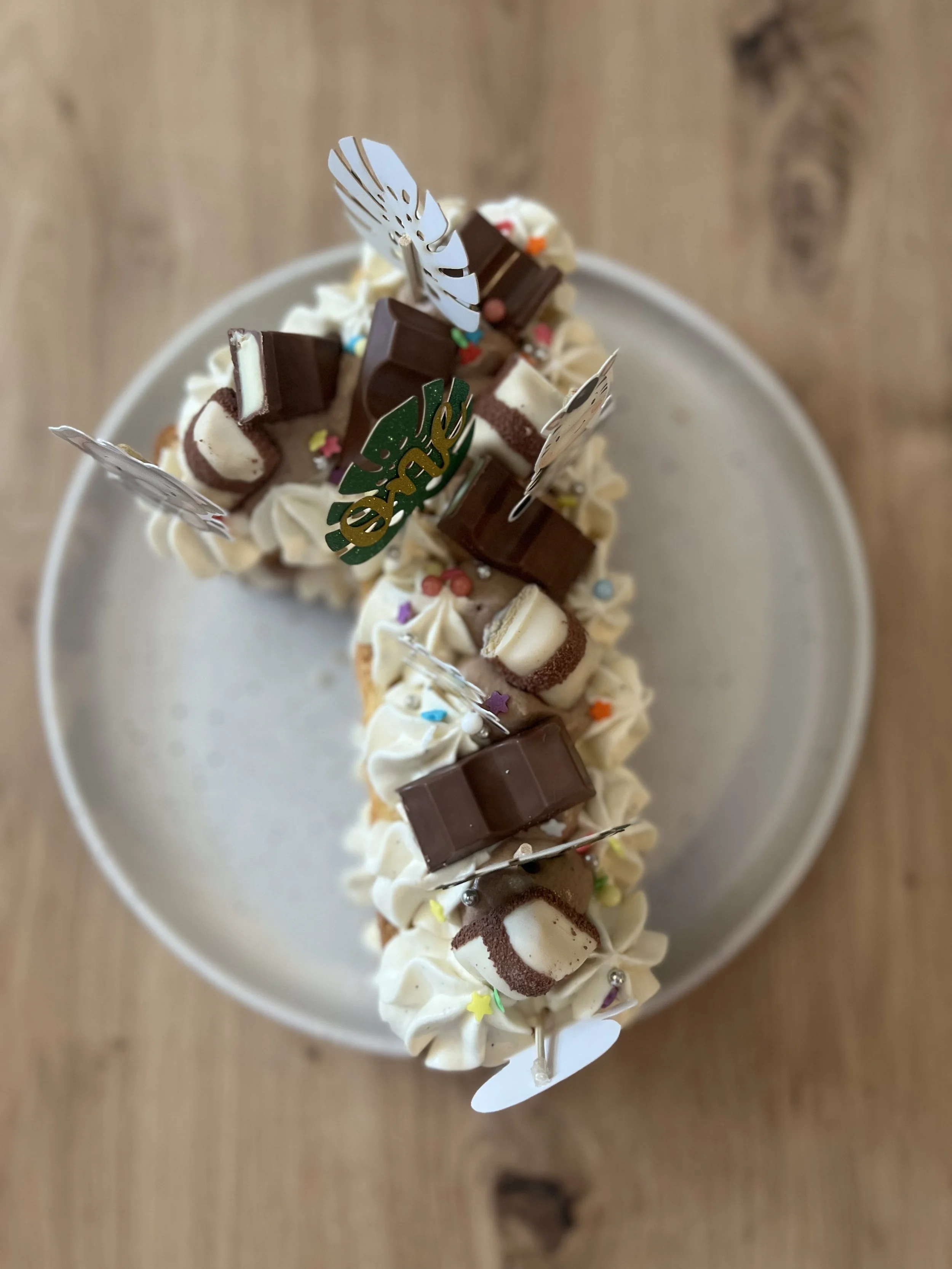 Gâteau de fête décoré de chocolat, petits bonbons colorés, avec des décorations en papier holographique et un message »one»