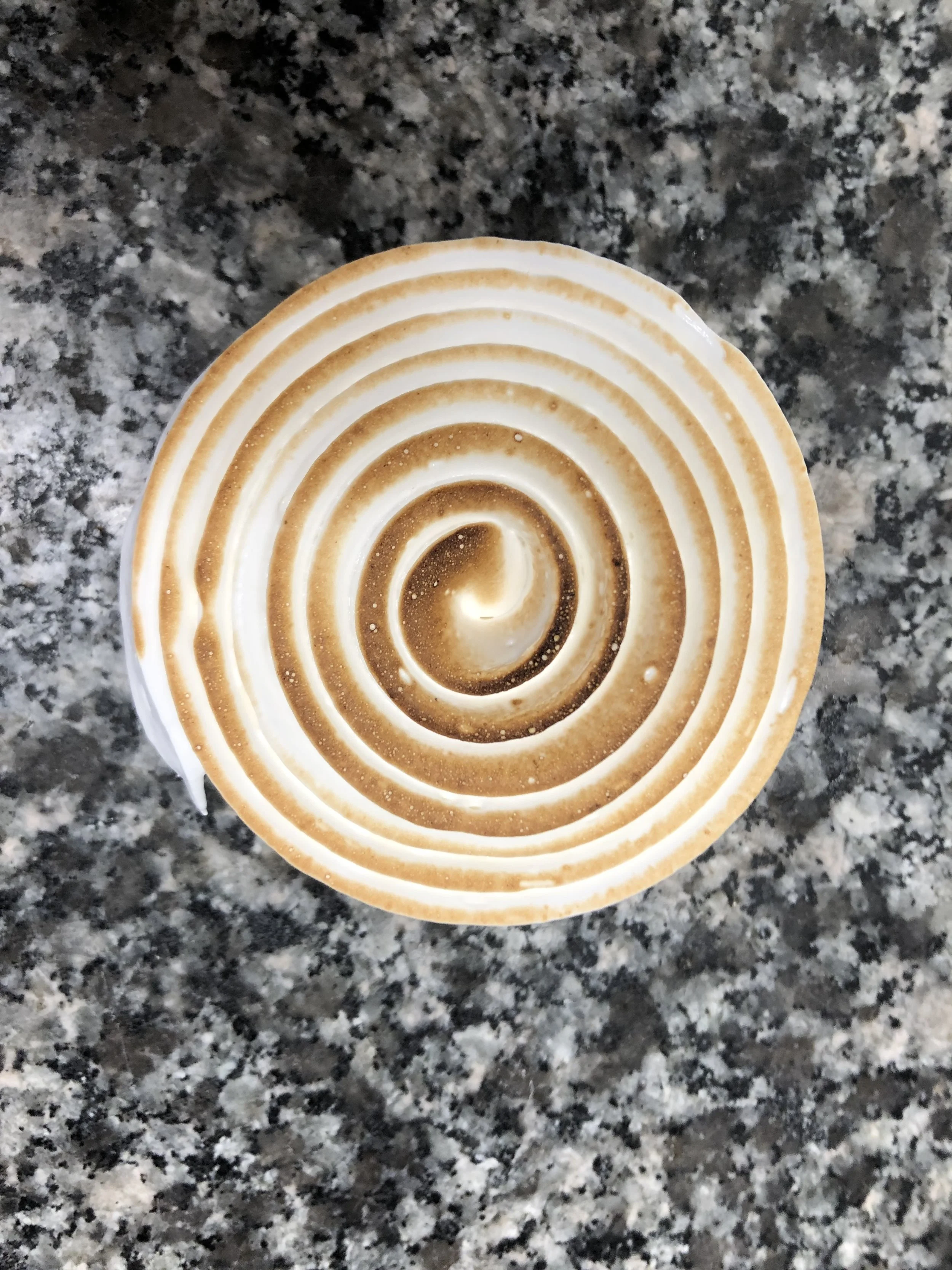 Un dessert en forme de spirale avec un glaçage marron clair et blanc, sur un comptoir en granite.