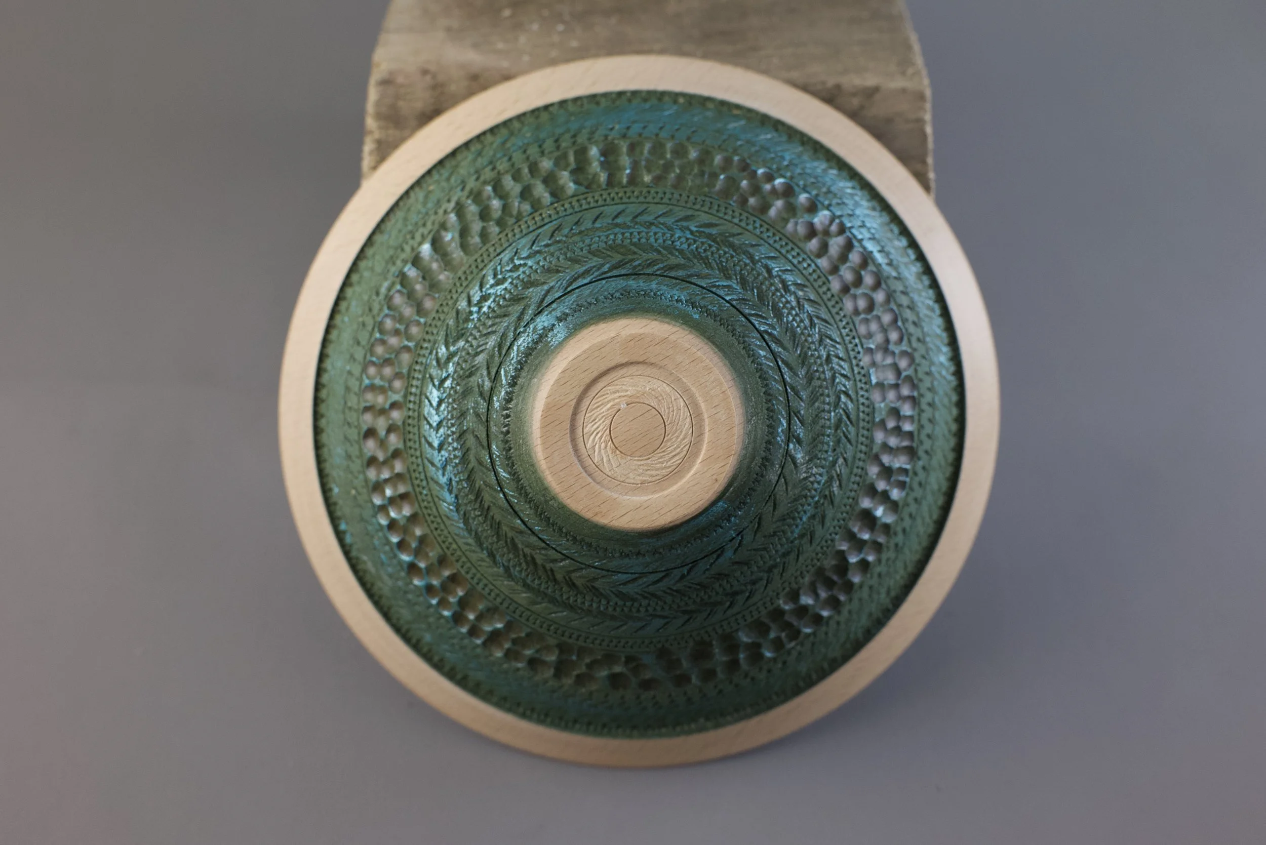 Close-up of the bottom of a round, decorative glass object with intricate patterns, set on a wooden stand against a gray background.