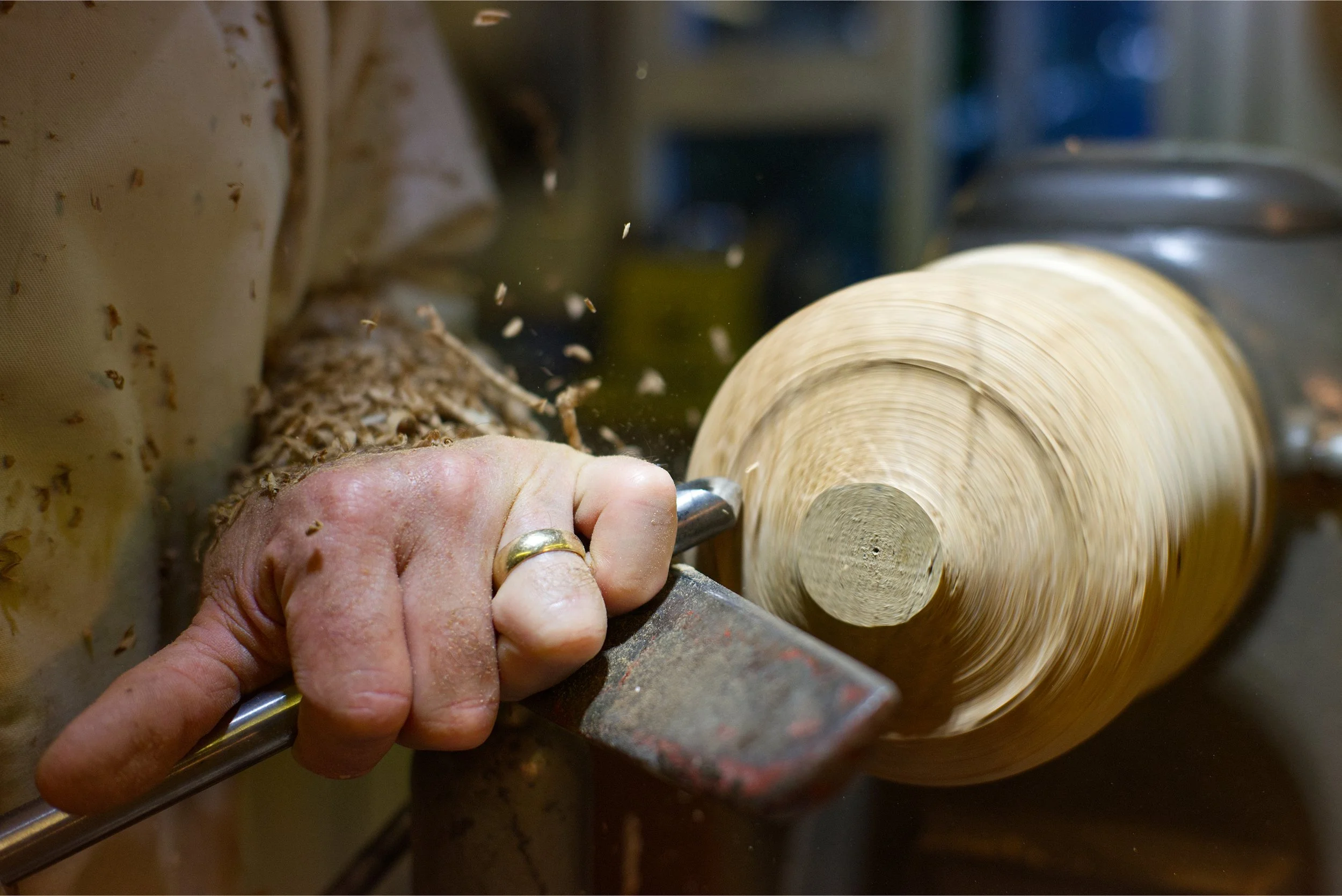 Close-up of a person's hand shaping a piece of wood on a lathe for woodturning.
