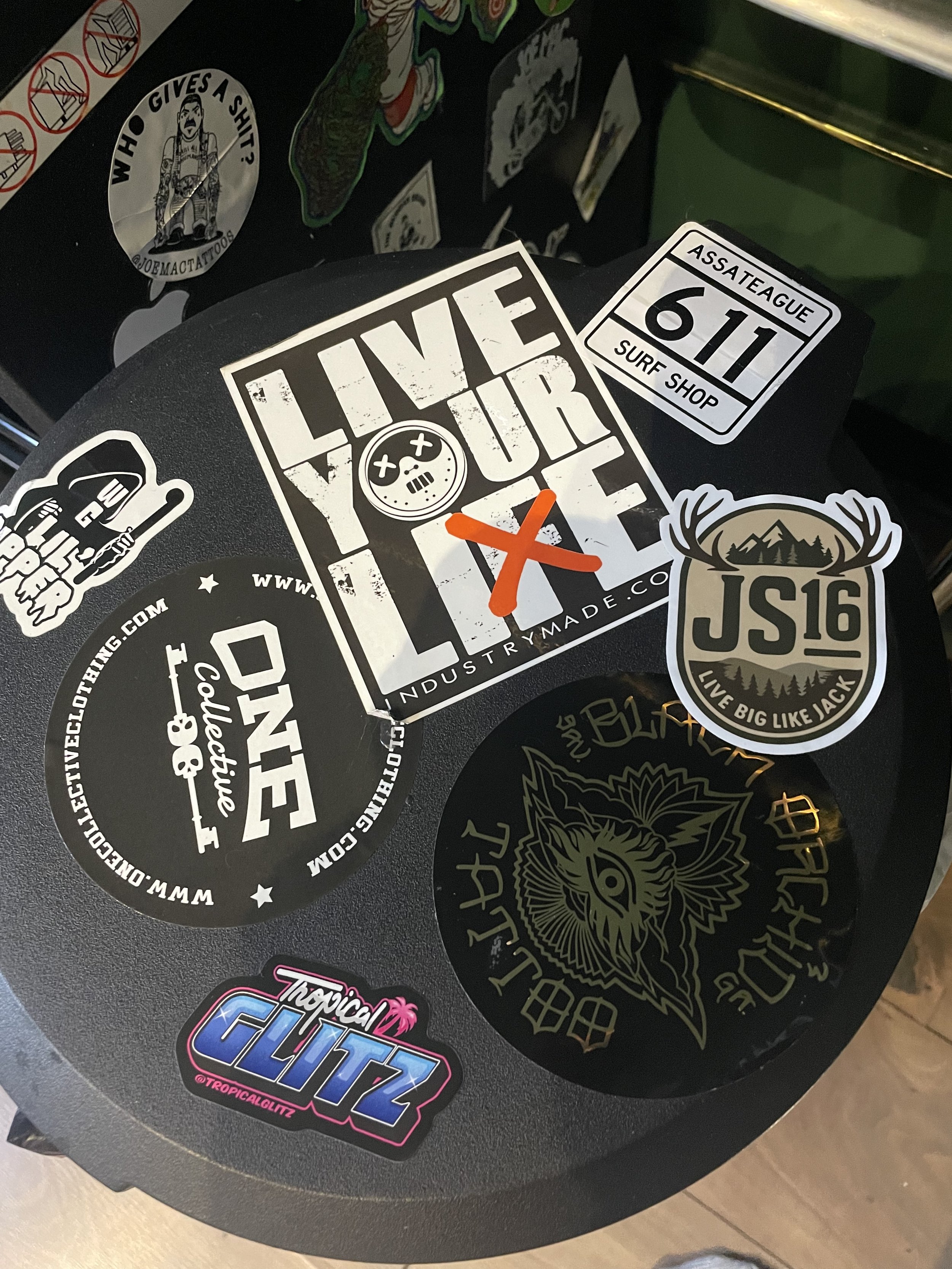 A collection of various stickers on a black surface, including vintage-style, cartoon, and text-based designs, with some promoting surfing and skateboard culture.