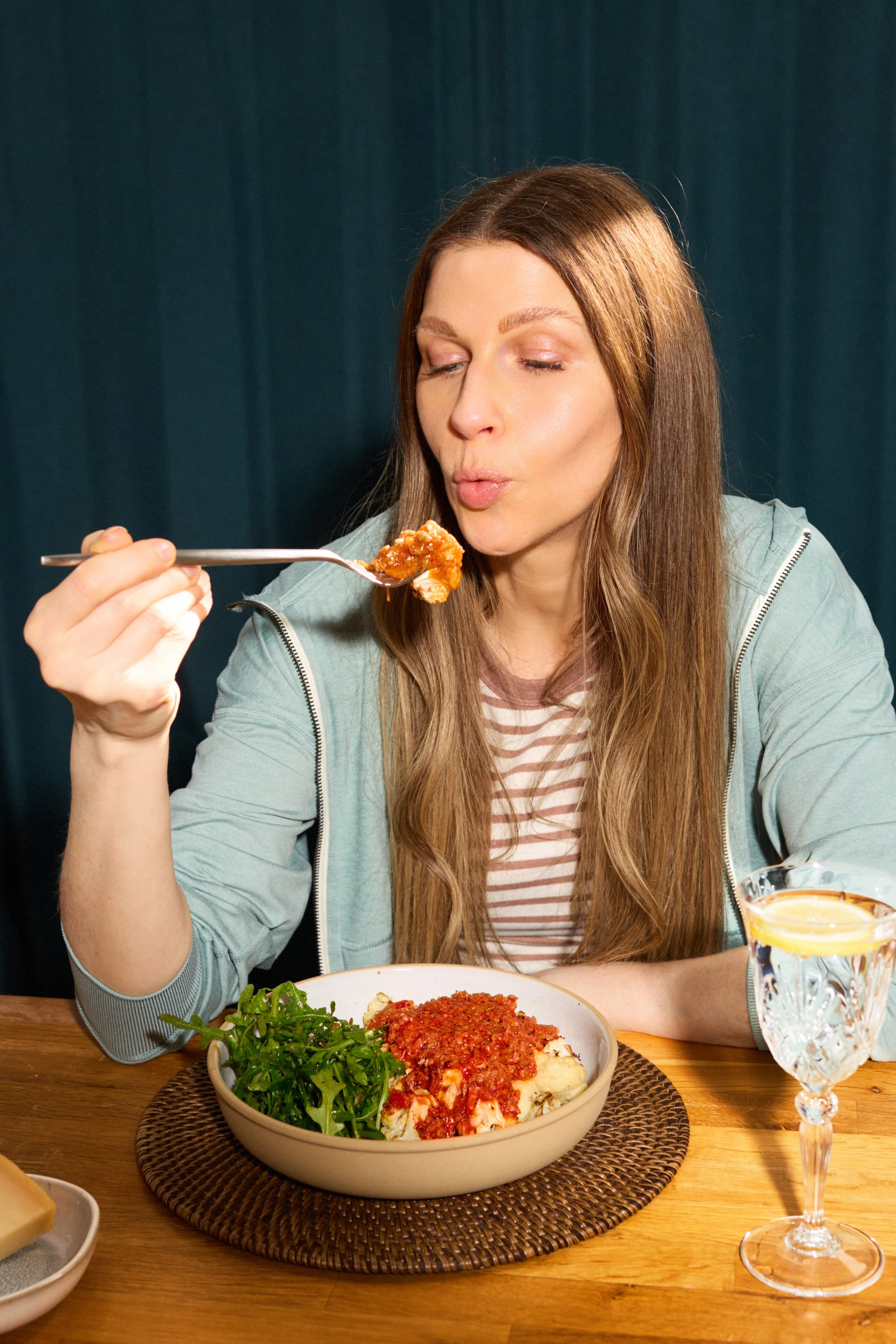 Sabine Venier wearing a light green zip-up hoodie eating food at a table with a dark blue background.