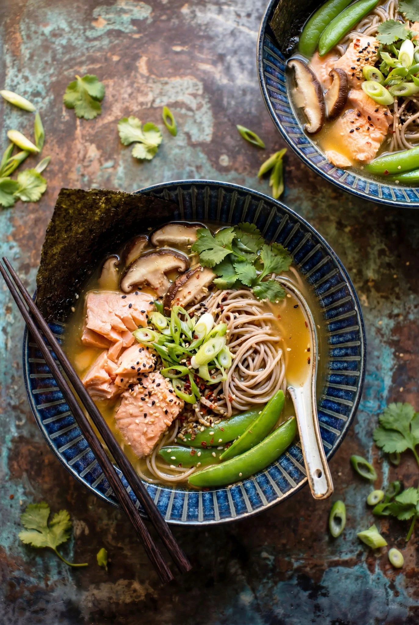Bowl of ramen with salmon, mushrooms, green onions, seaweed, and sesame seeds on a rustic surface.