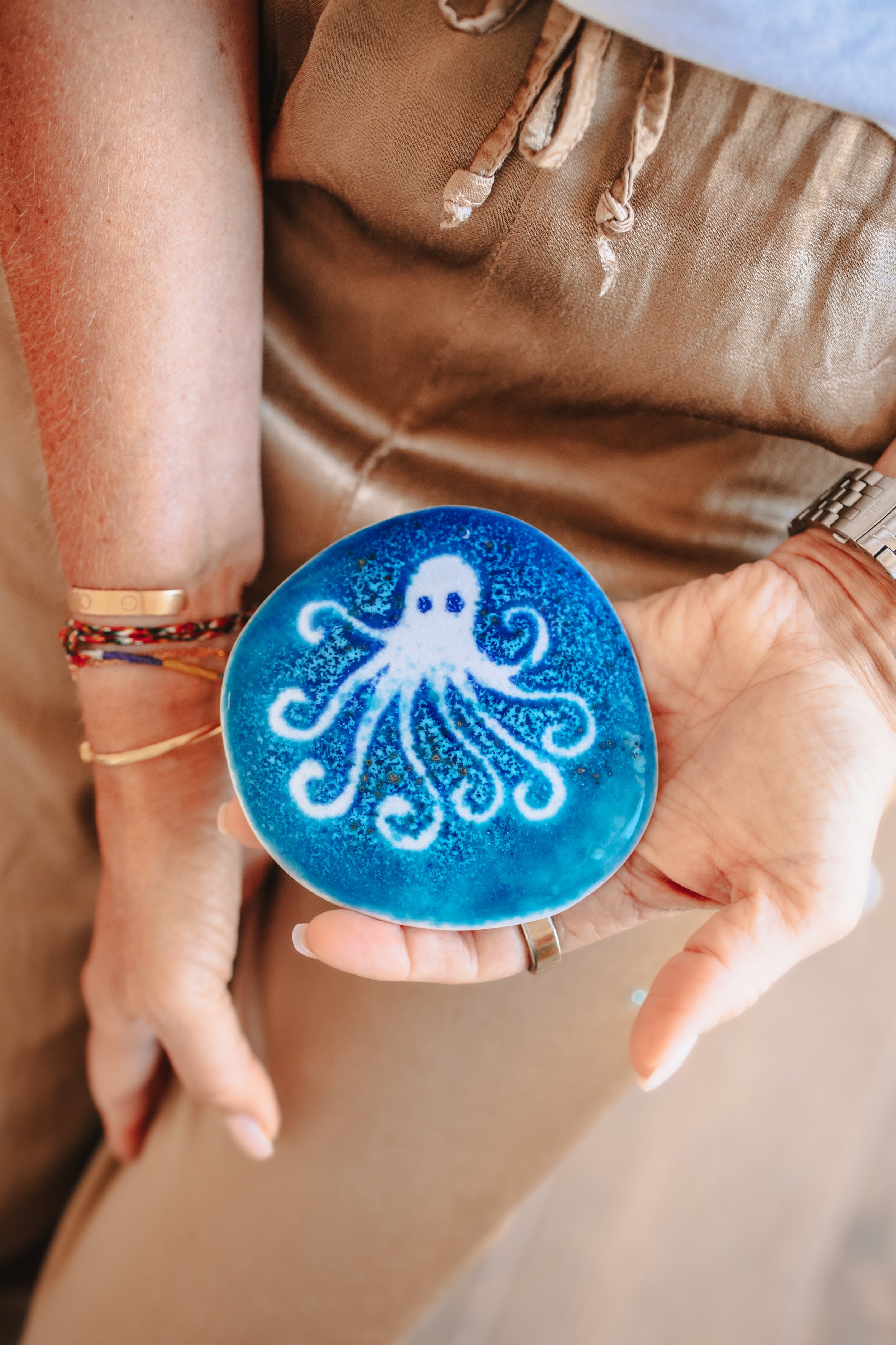 Andrea Flammuth hält ein bläulich-weißes Kunstwerk mit einem Tintenfischmuster, das auf eine runde Platte aufgetragen ist.