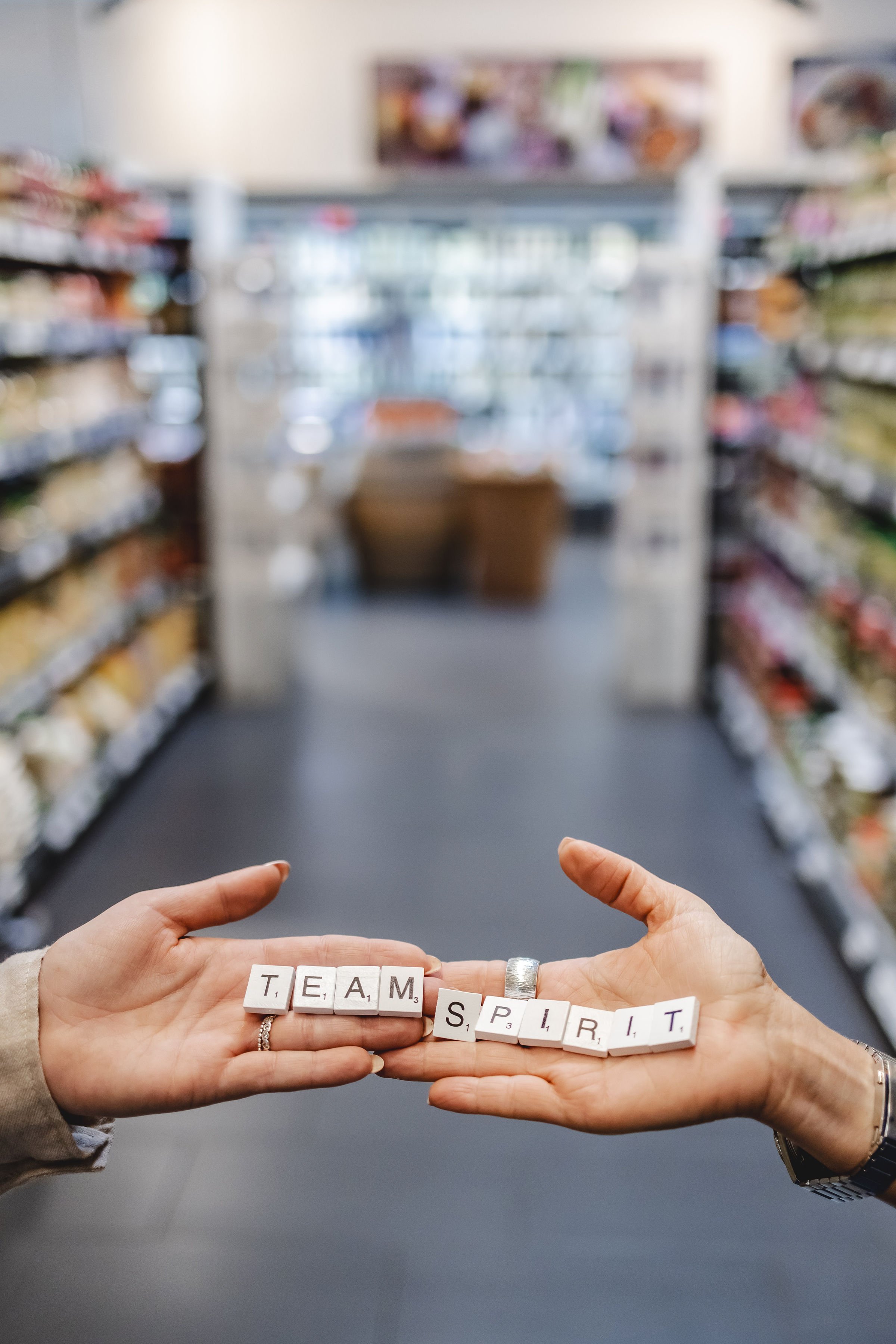 Zwei Hände halten Zeichen mit dem Text 'TEAM SPIRIT' im Supermarkt.