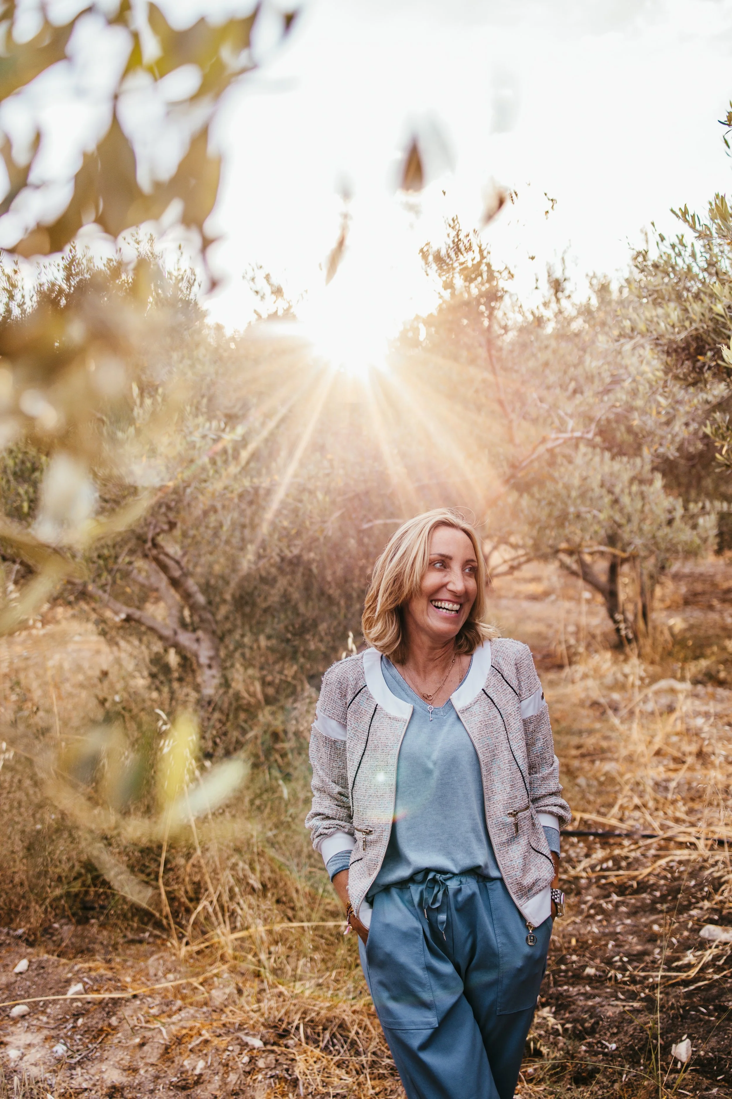 Eine lachende Frau geht am Nachmittag durch einen Olivenhain.