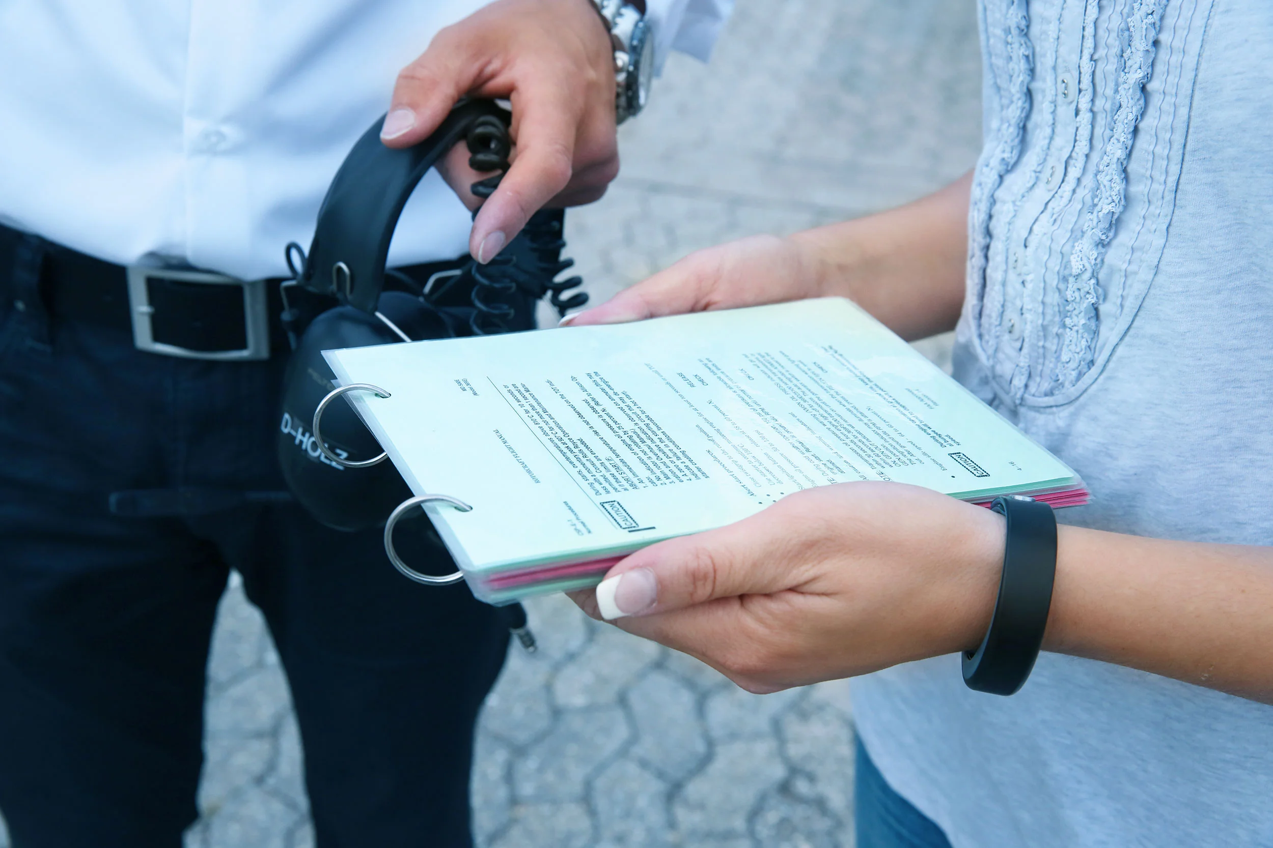 Zwei Menschen, die Dokumente und Kopfhörer im Freien halten, vermutlich im Gespräch.