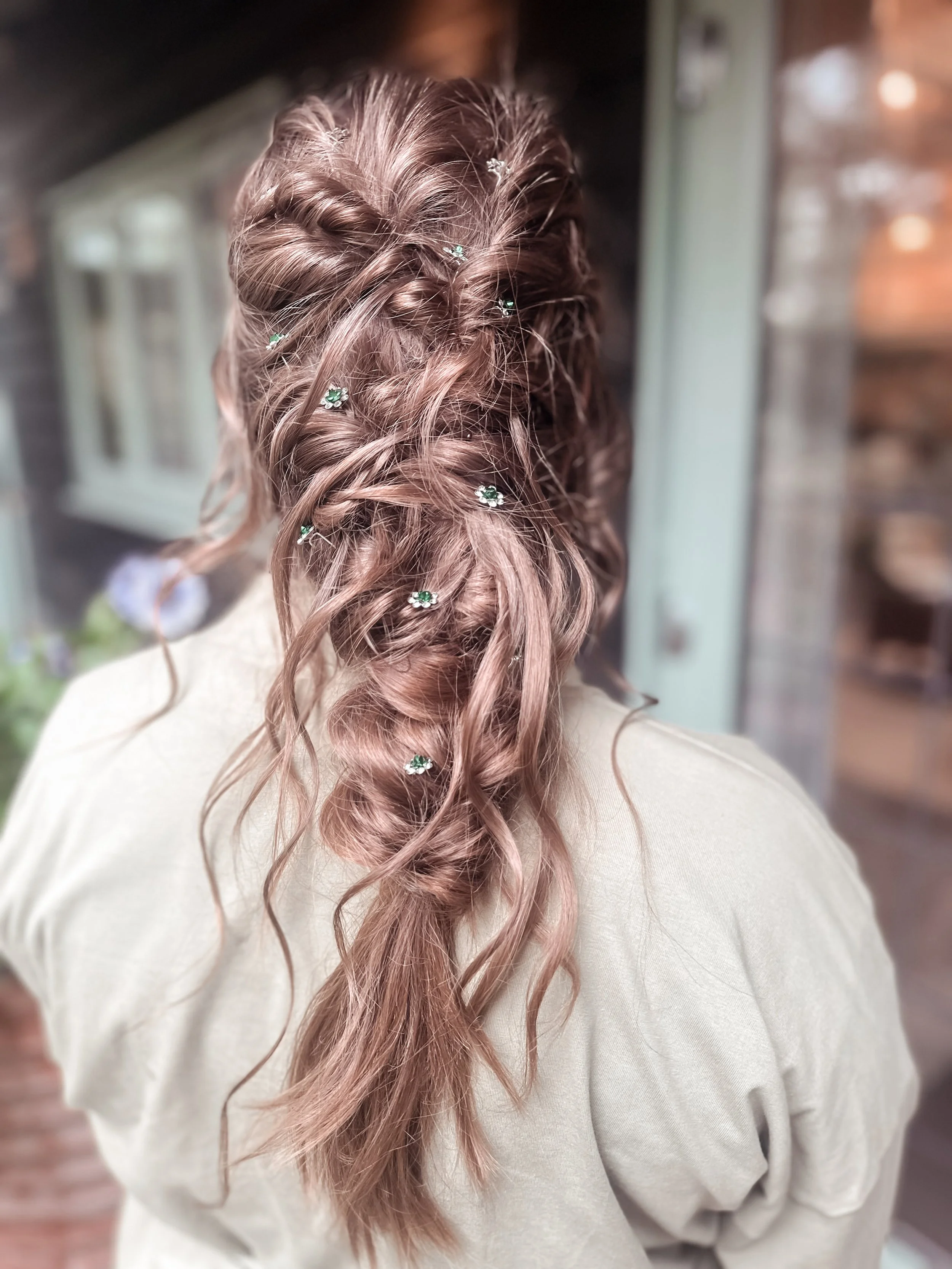 Back view of a woman with long, wavy, light brown hair styled with small floral hair accessories.