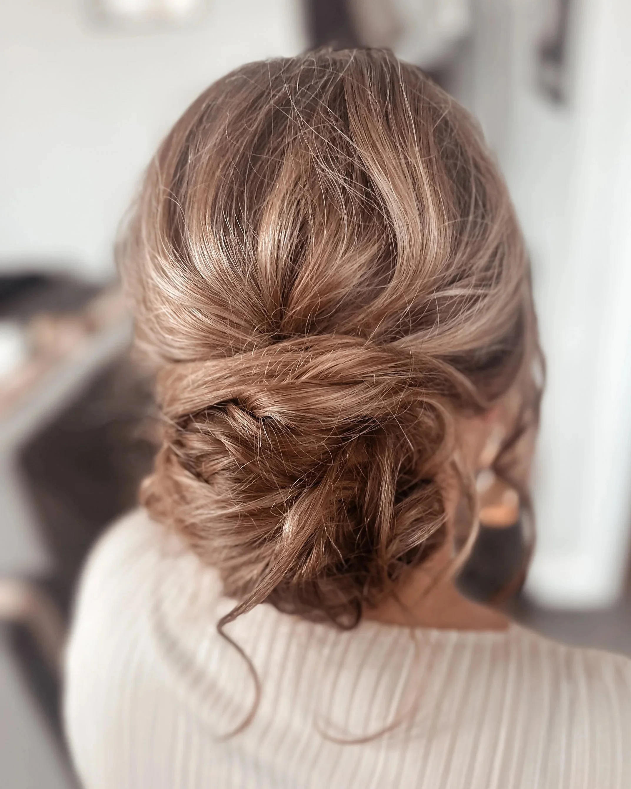 A woman with brown, wavy hair styled in an elegant updo, viewed from the back.