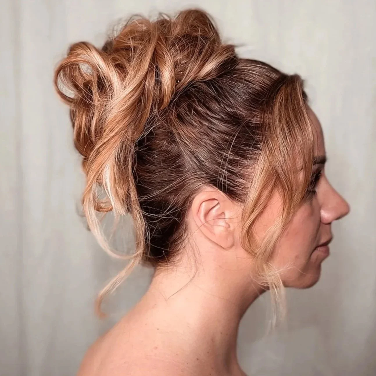 Side view of a woman with an elaborate updo hairstyle with loose curls and light brown and blonde hair color.