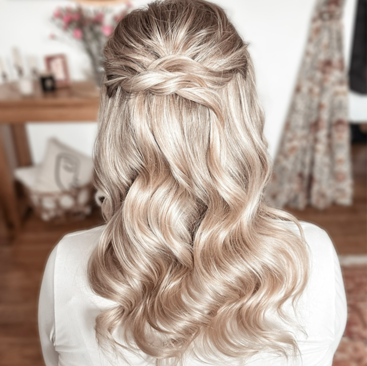 Back view of a woman with styled blonde hair featuring loose curls and a twisted braid across the crown.