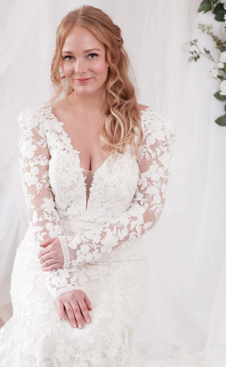 A woman with long, curly blonde hair wearing a white lace wedding dress.