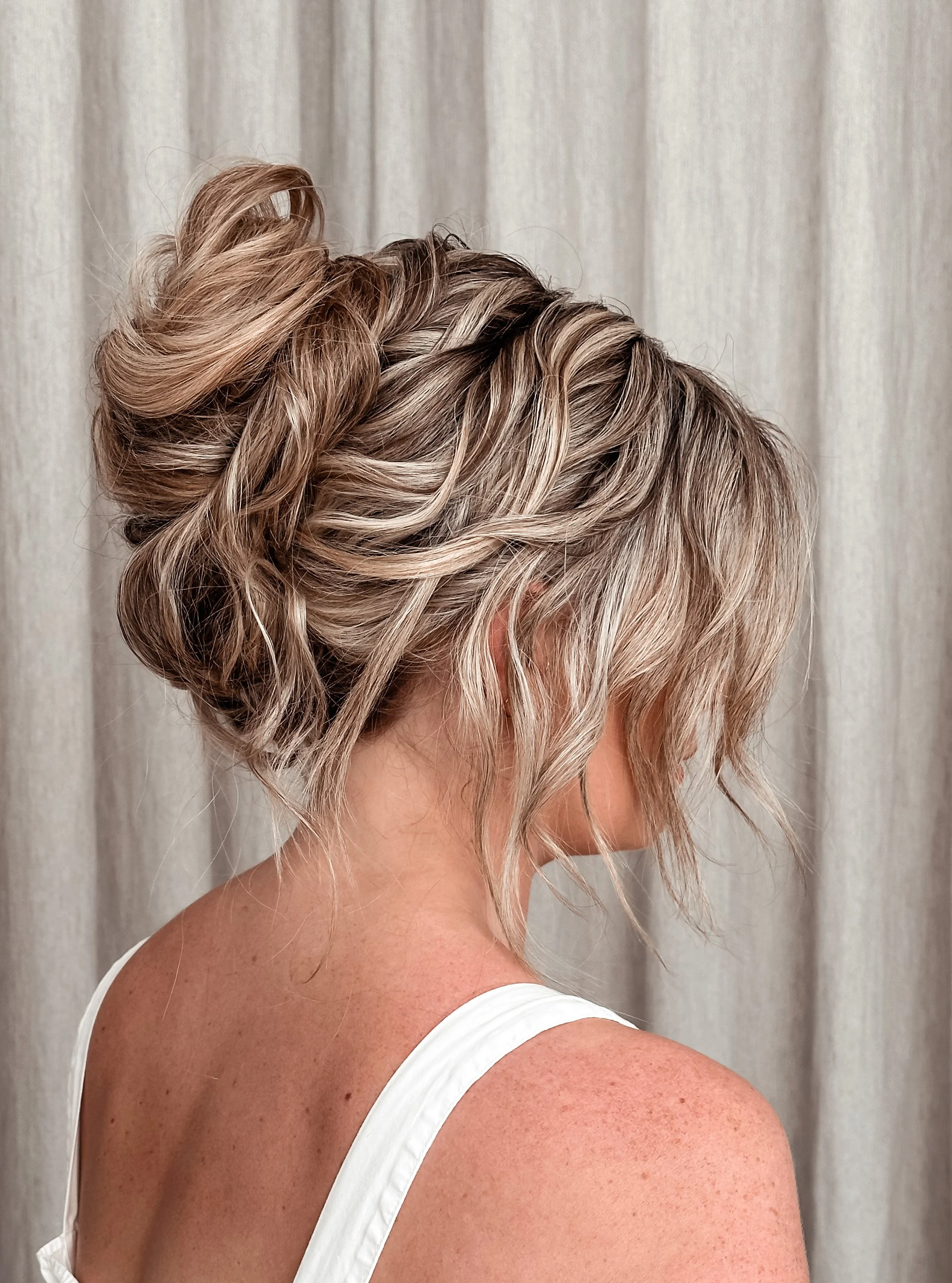 A woman with short, wavy blonde hair styled in an intricate updo with curls and twists