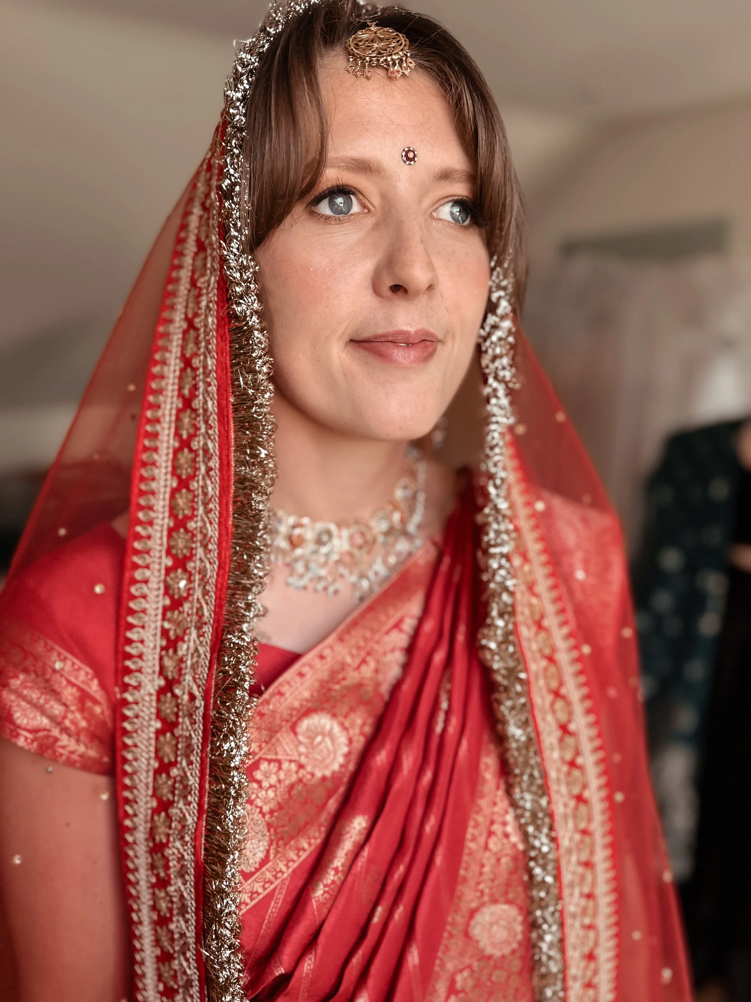 A woman in traditional Indian attire, including a red saree with gold patterns, silver jewelry, and a red dupatta with silver embellishments, looking slightly to the side.