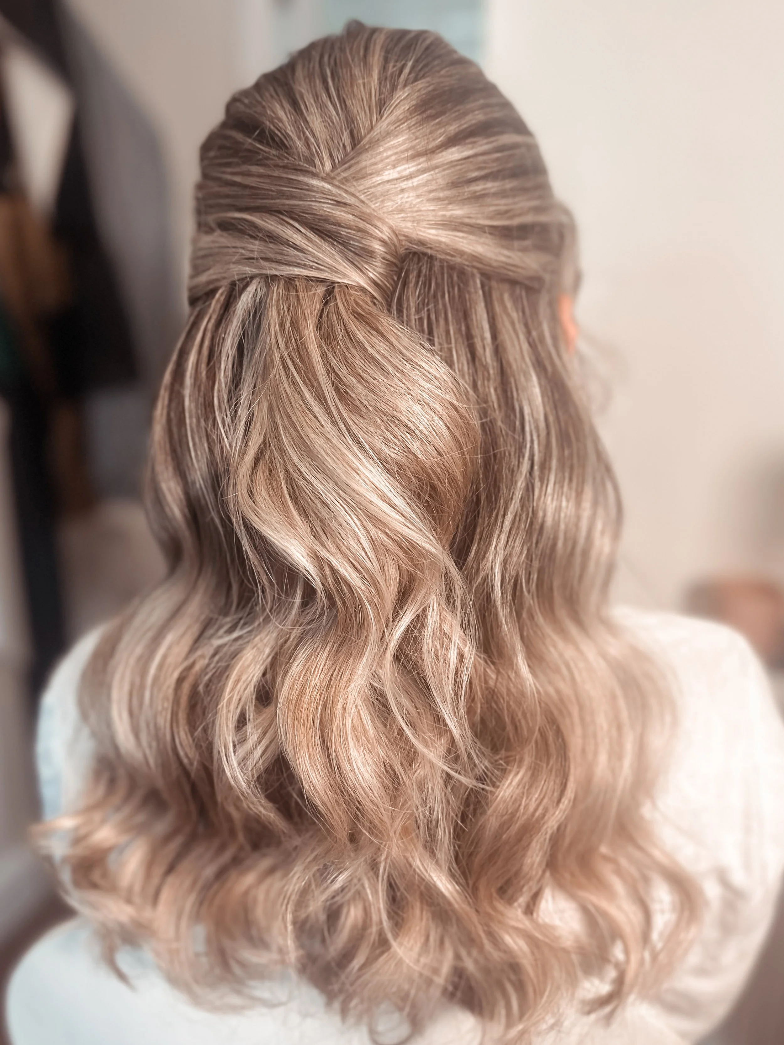 Back view of a woman with blonde, wavy hair styled in loose curls.