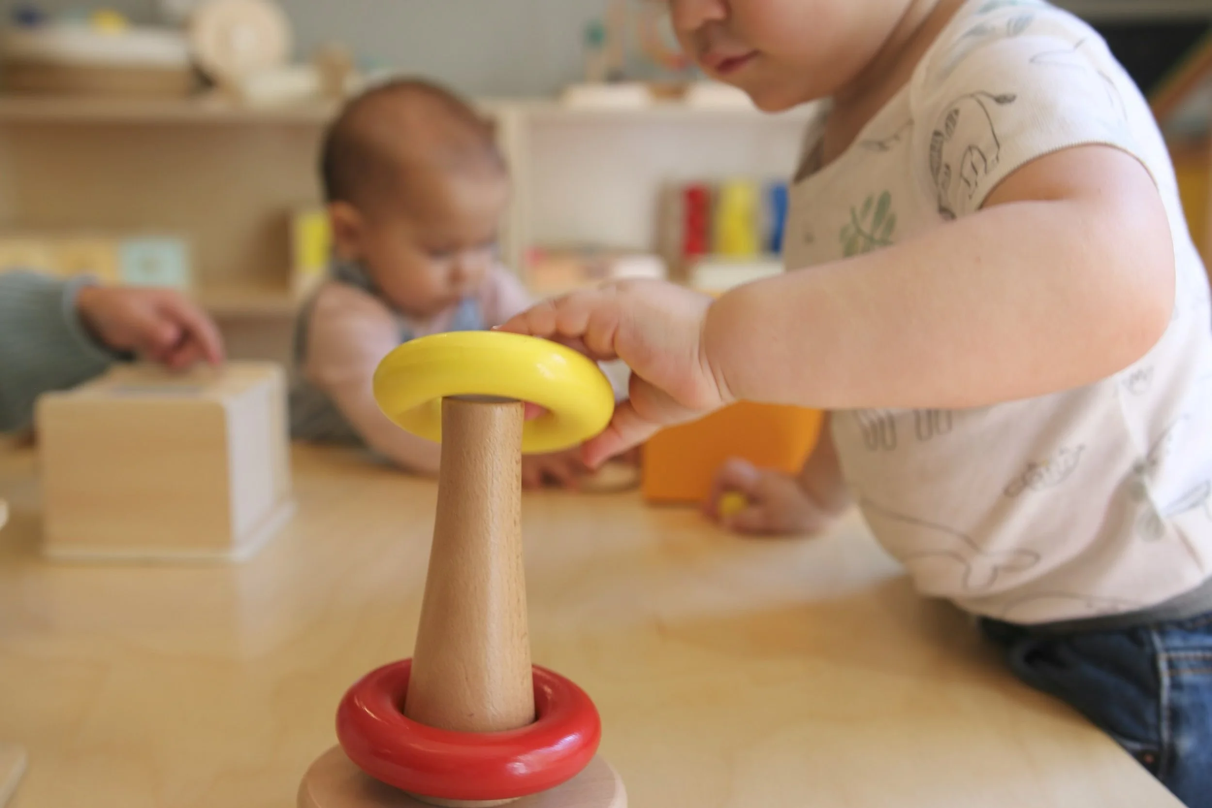Close-up of two young children playing with a wooden ring stacker toy, with the focus on the colorful rings and the child's hand.