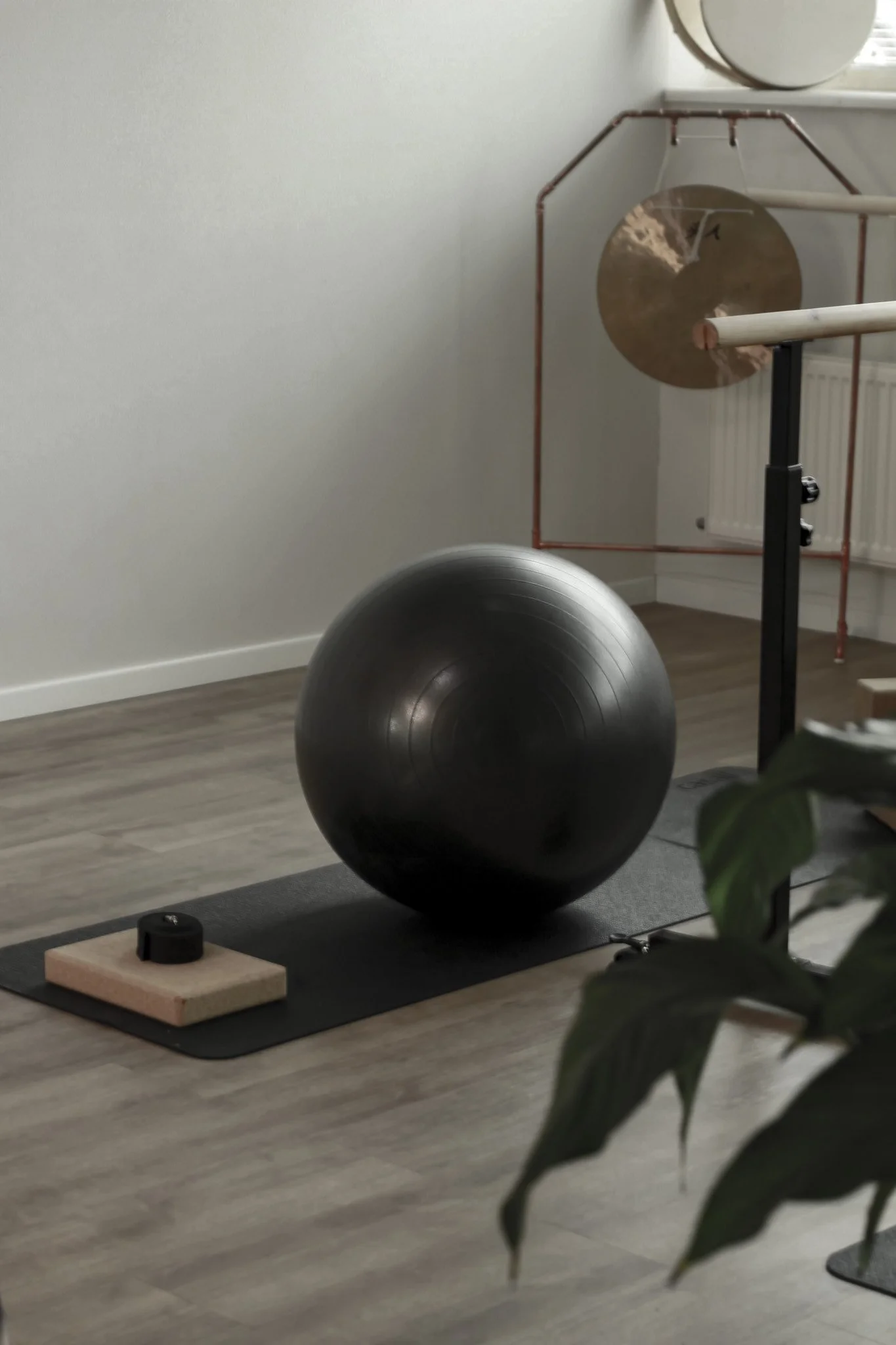 Home gym with a black exercise ball, yoga mat, cork blocks, and a large brass gong in the background.