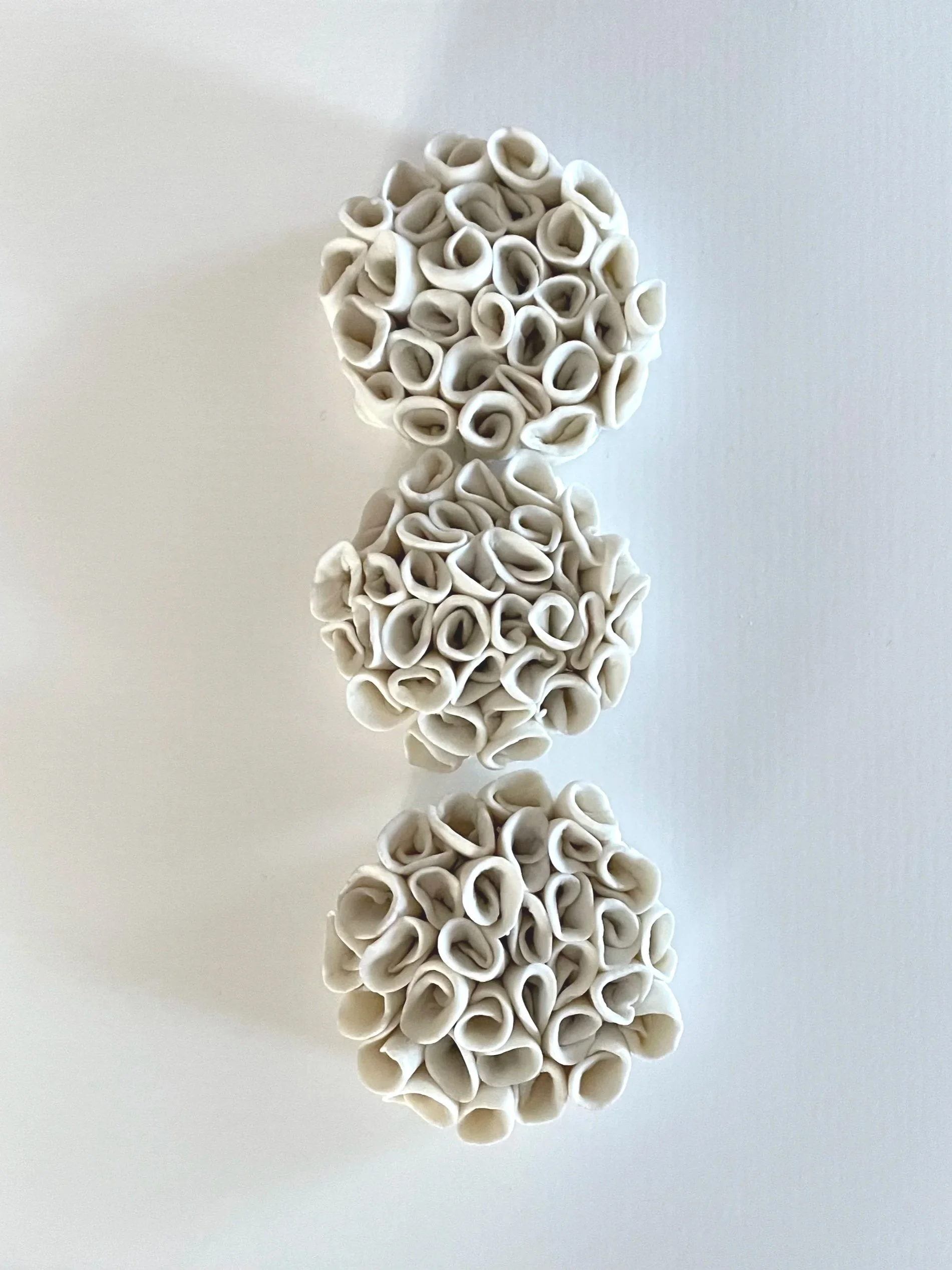 Three white, curled, flower-like objects stacked vertically on a white background.