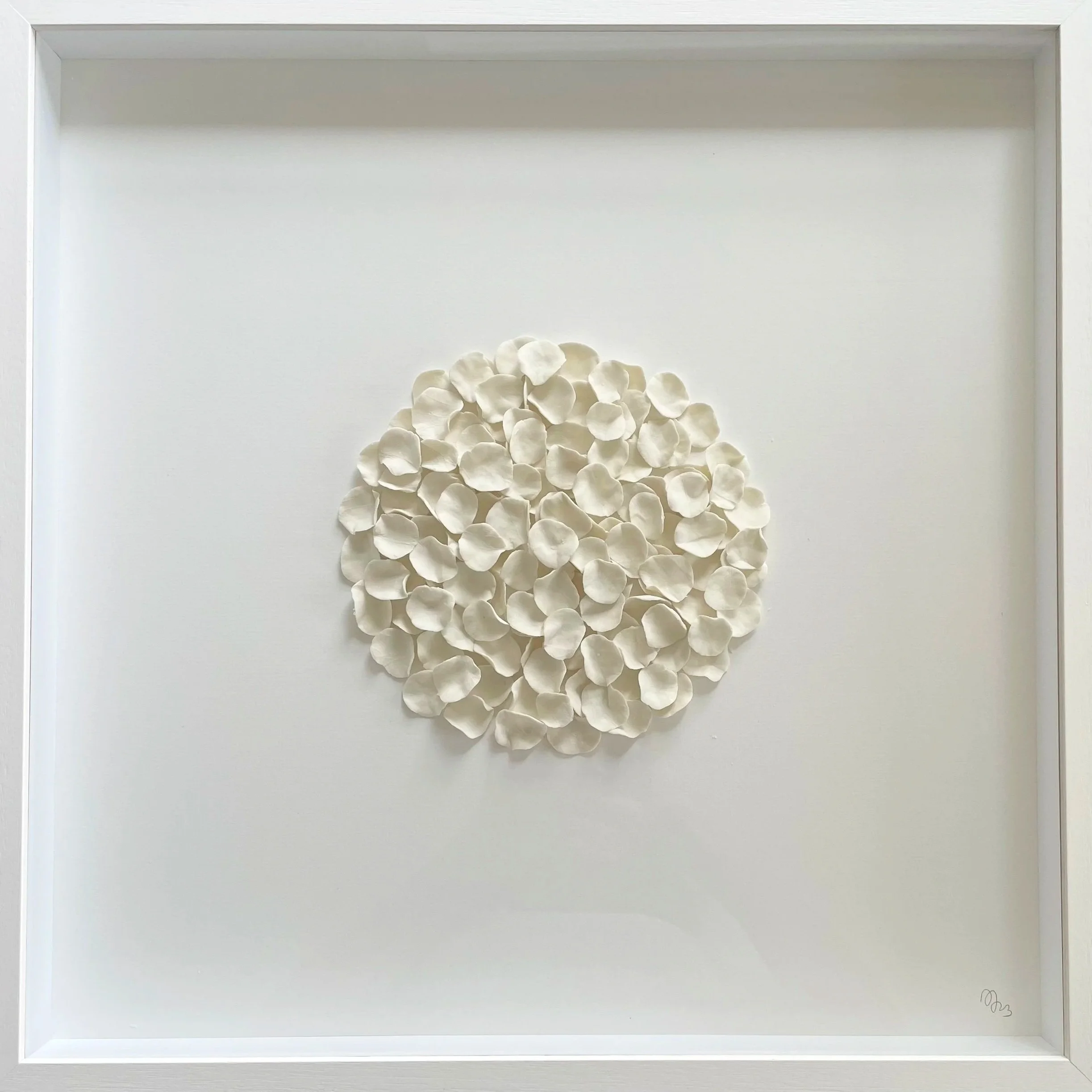 White circular art piece made of layered paper or fabric petals on a white background with a white frame.