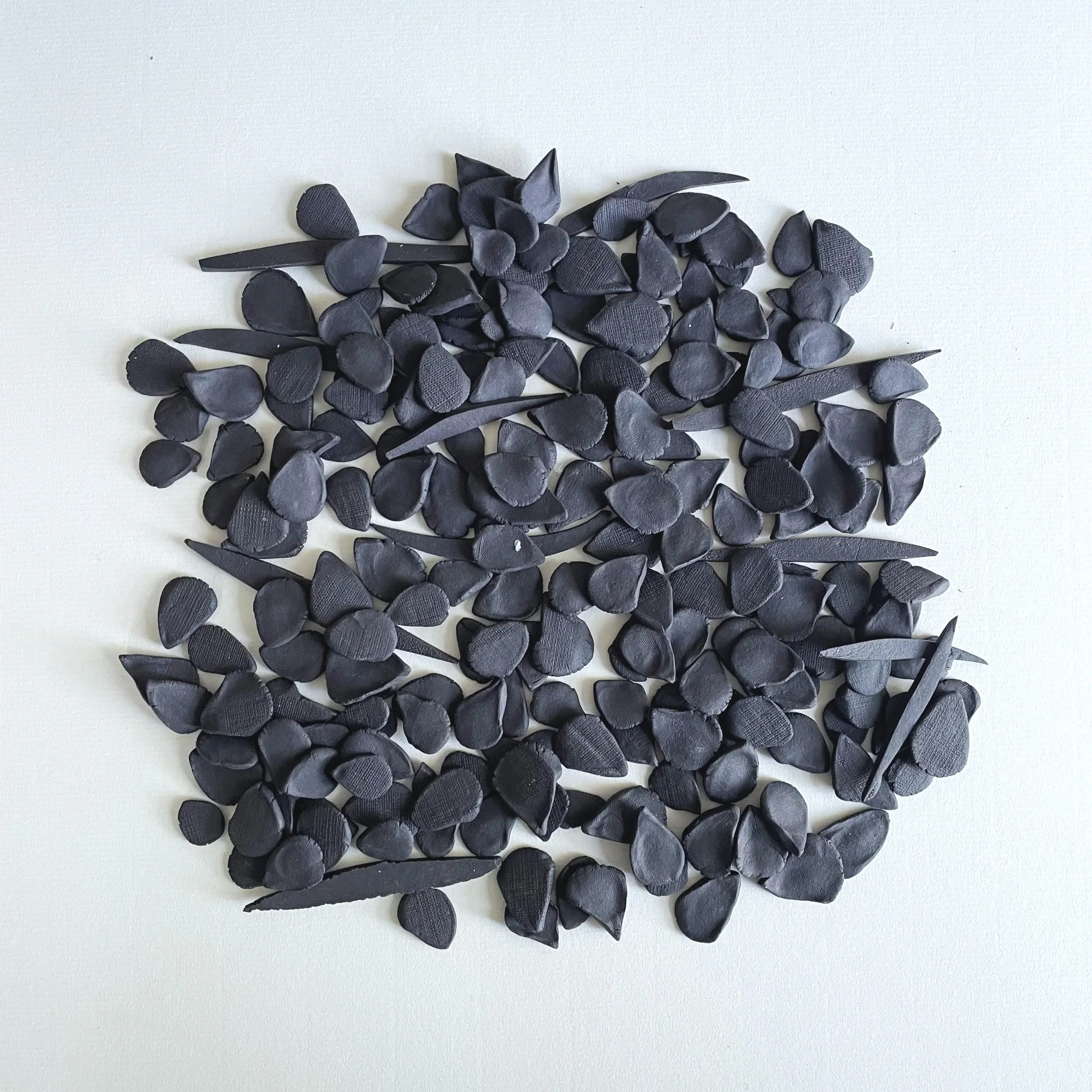 Collection of artificial black flower petals and leaves arranged on a white background.