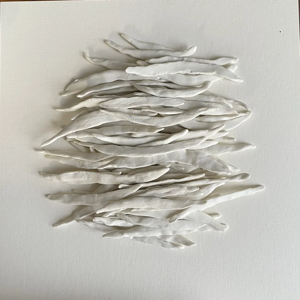 An abstract art piece made of white, elongated, twisted, and layered ceramic or plaster pieces arranged in a diamond shape on a light-colored wall.