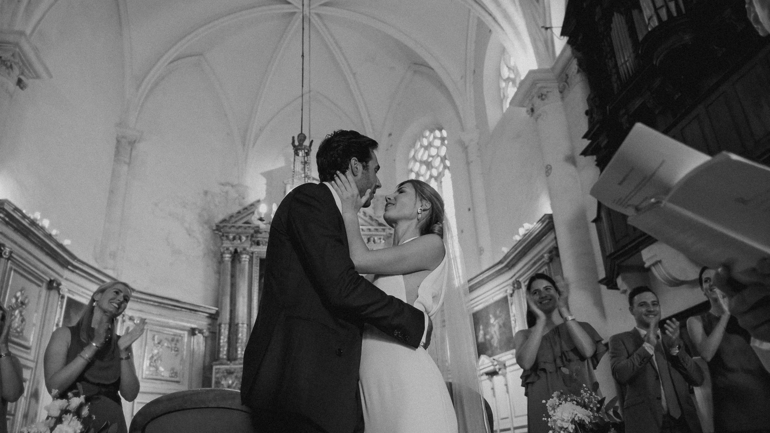 Un couple qui se marie danse et se regarde avec amour dans une église, entouré de témoins heureux.