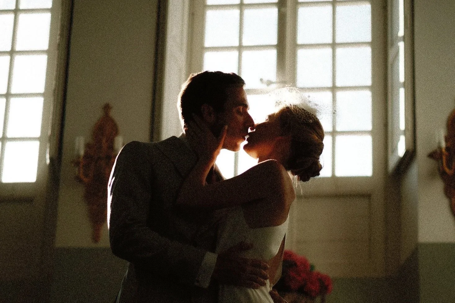 Un couple s'embrassant dans une pièce éclairée par des fenêtres lumineuses, avec un décor classique.
