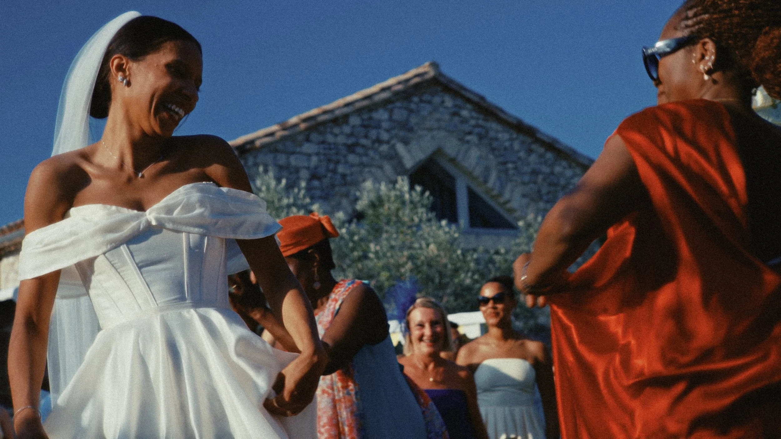 Un groupe de personnes souriantes et habillées en tenues colorées lors d'une célébration extérieure, sous un ciel bleu clair.